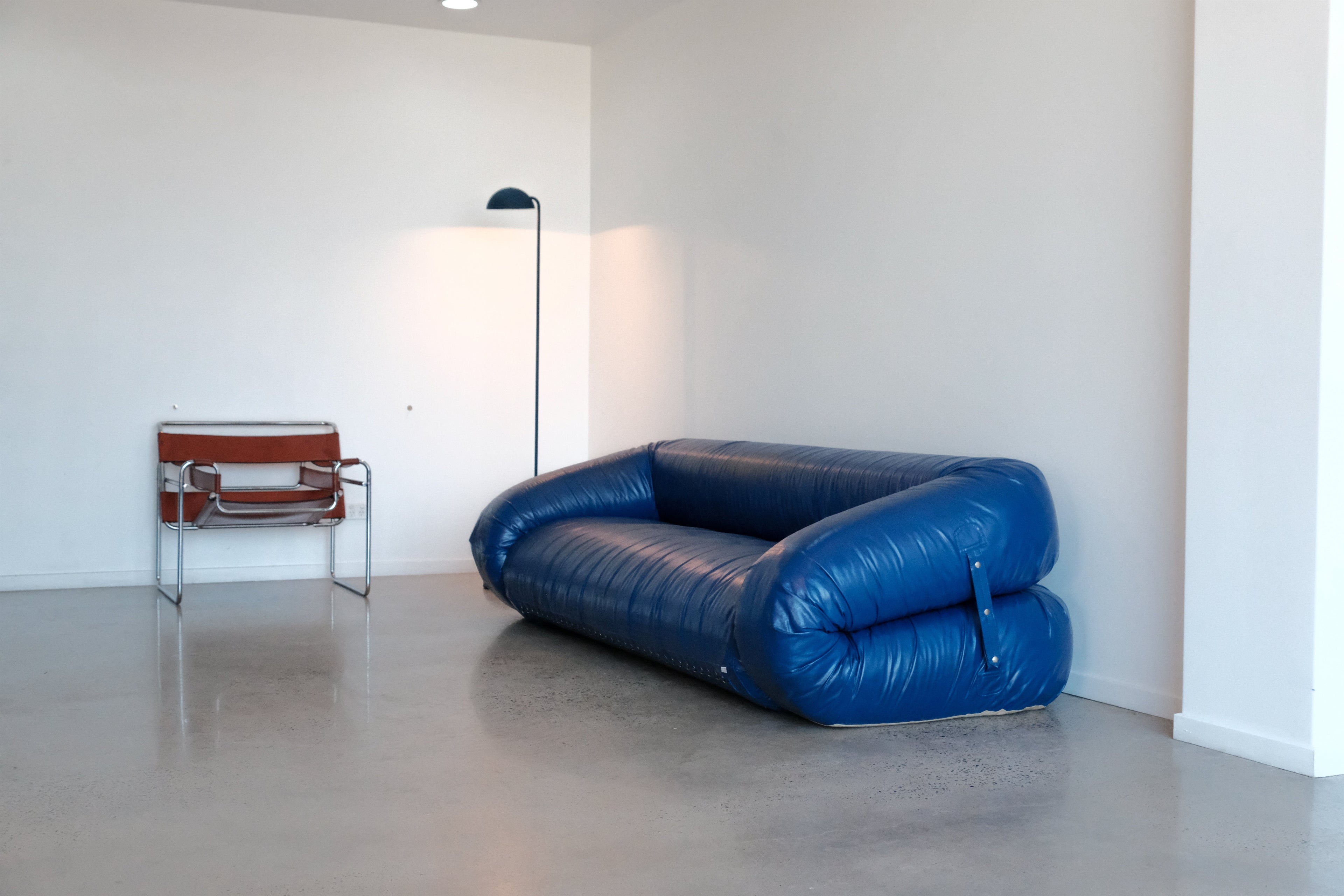 Anfibio Blue sofa in a minimalistic room with a white wall and gray floor.