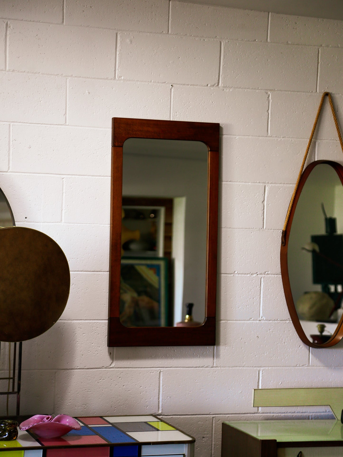 Three mirrors of different shapes and sizes on a white tiled wall.