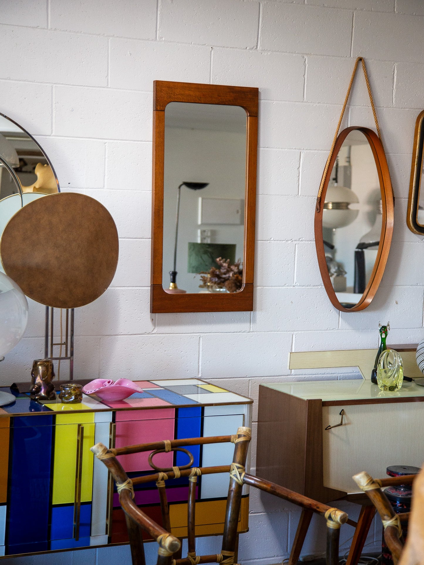 Colorful geometric-patterned cabinet with various mirrors on a tiled wall.