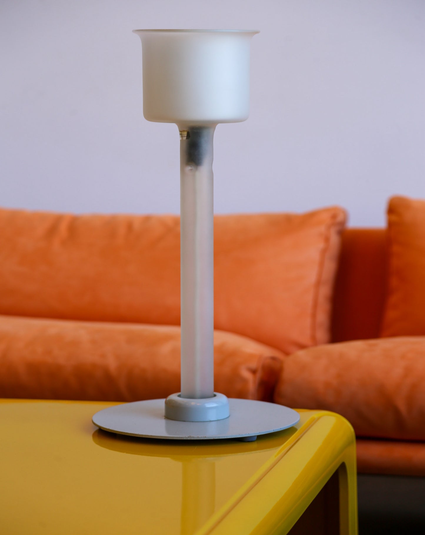 White lamp on a yellow table with an orange couch in the background