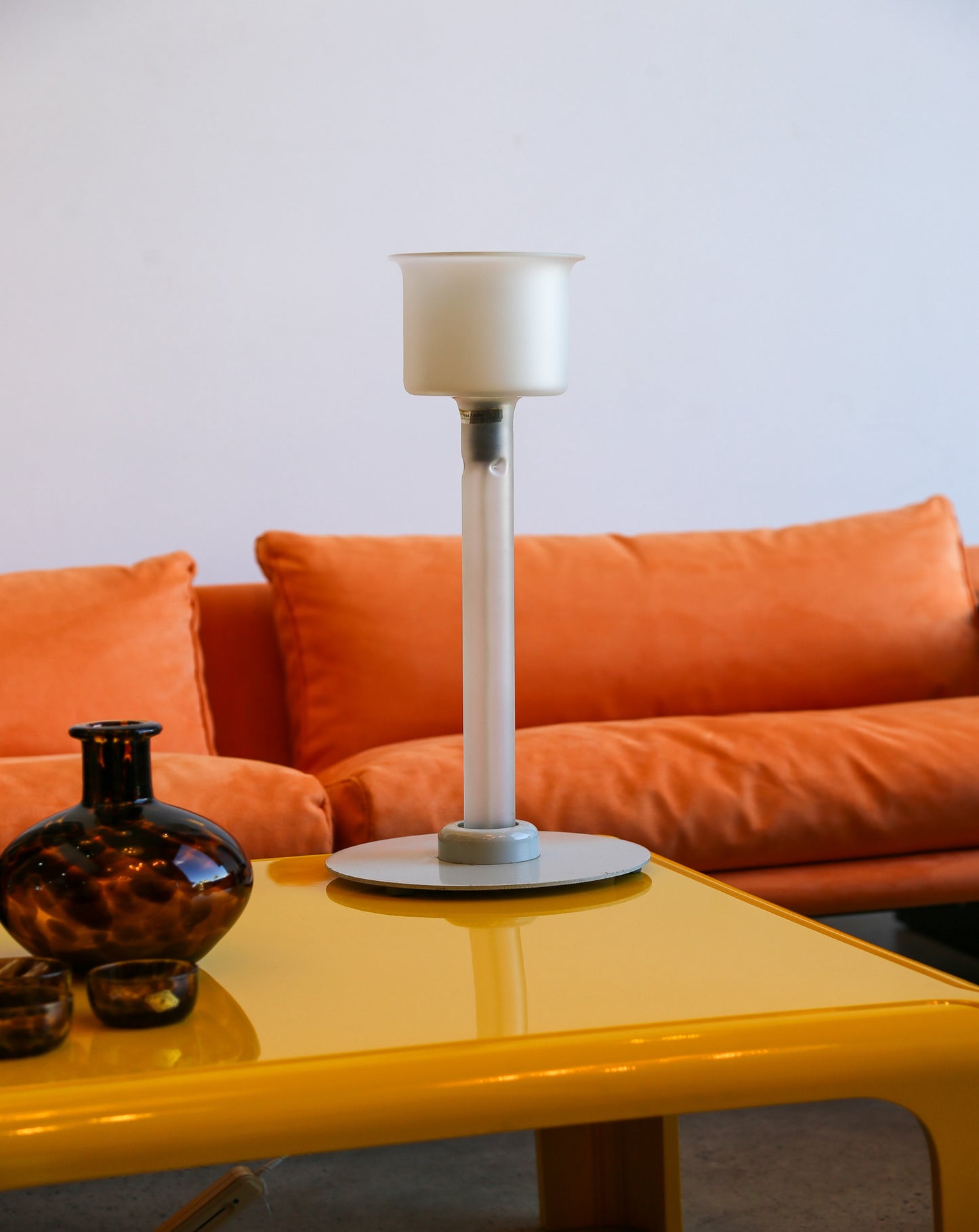 White lamp on a yellow table with an orange sofa in the background