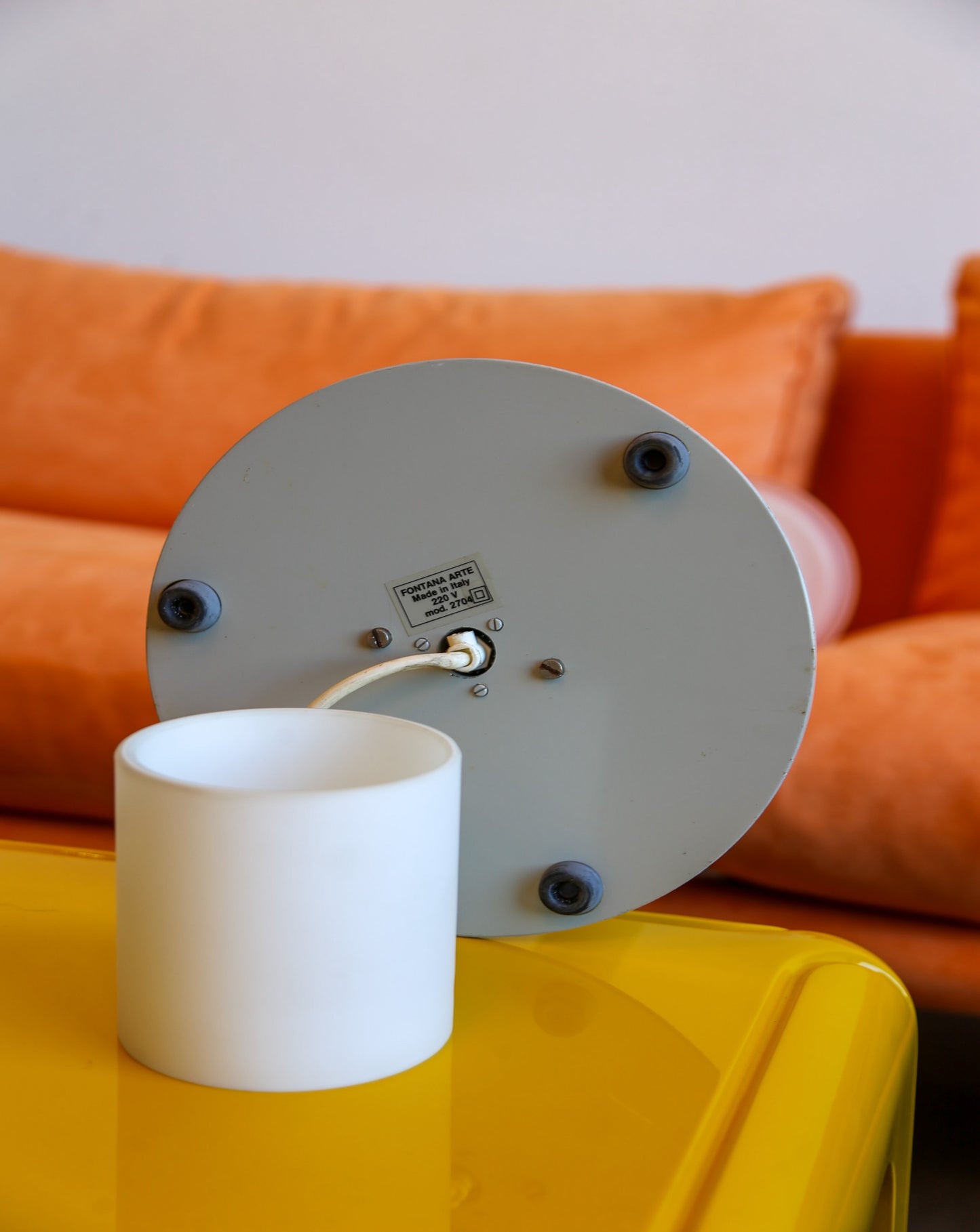 White lampshade on a yellow table with an orange sofa in the background
