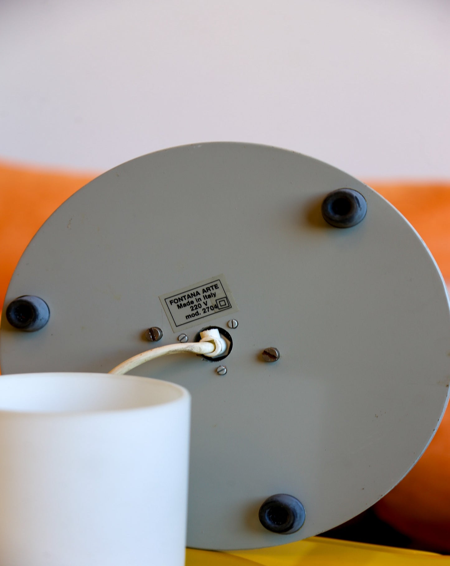 Close-up of a wall-mounted light fixture with visible brand label on an orange and yellow background.