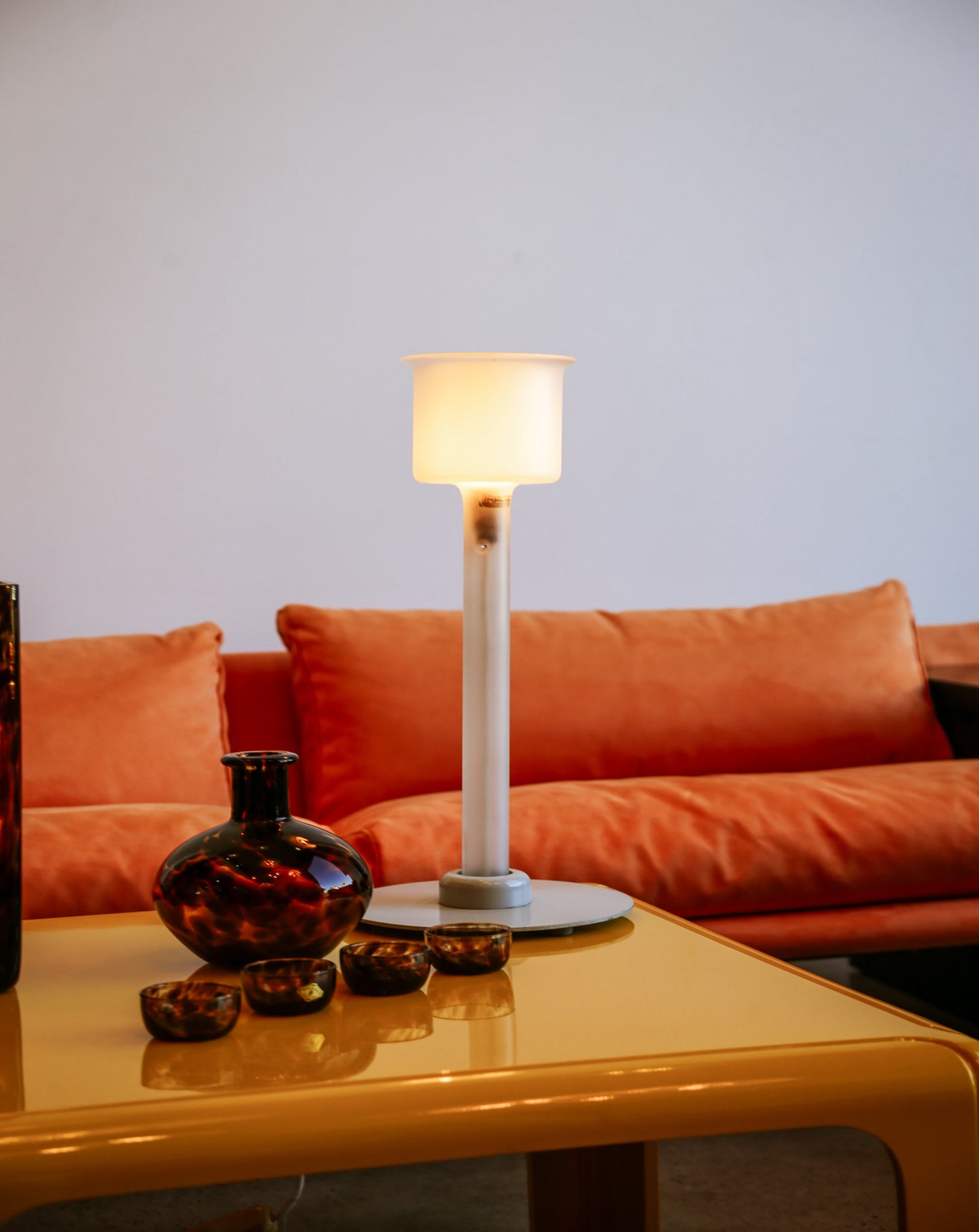 Orange sofa with a lamp and decorative items on a yellow table against a light blue wall.