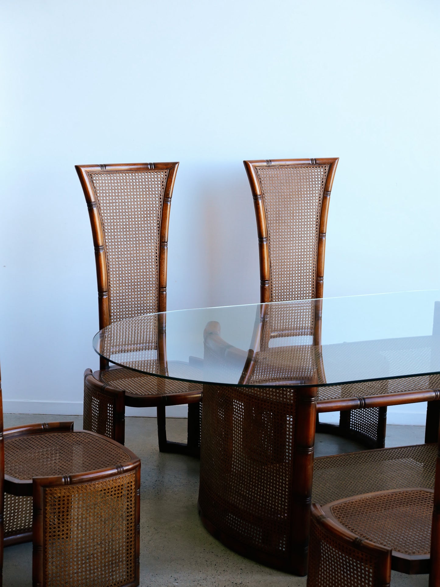 Dining table with glass top and four matching chairs against a white wall.