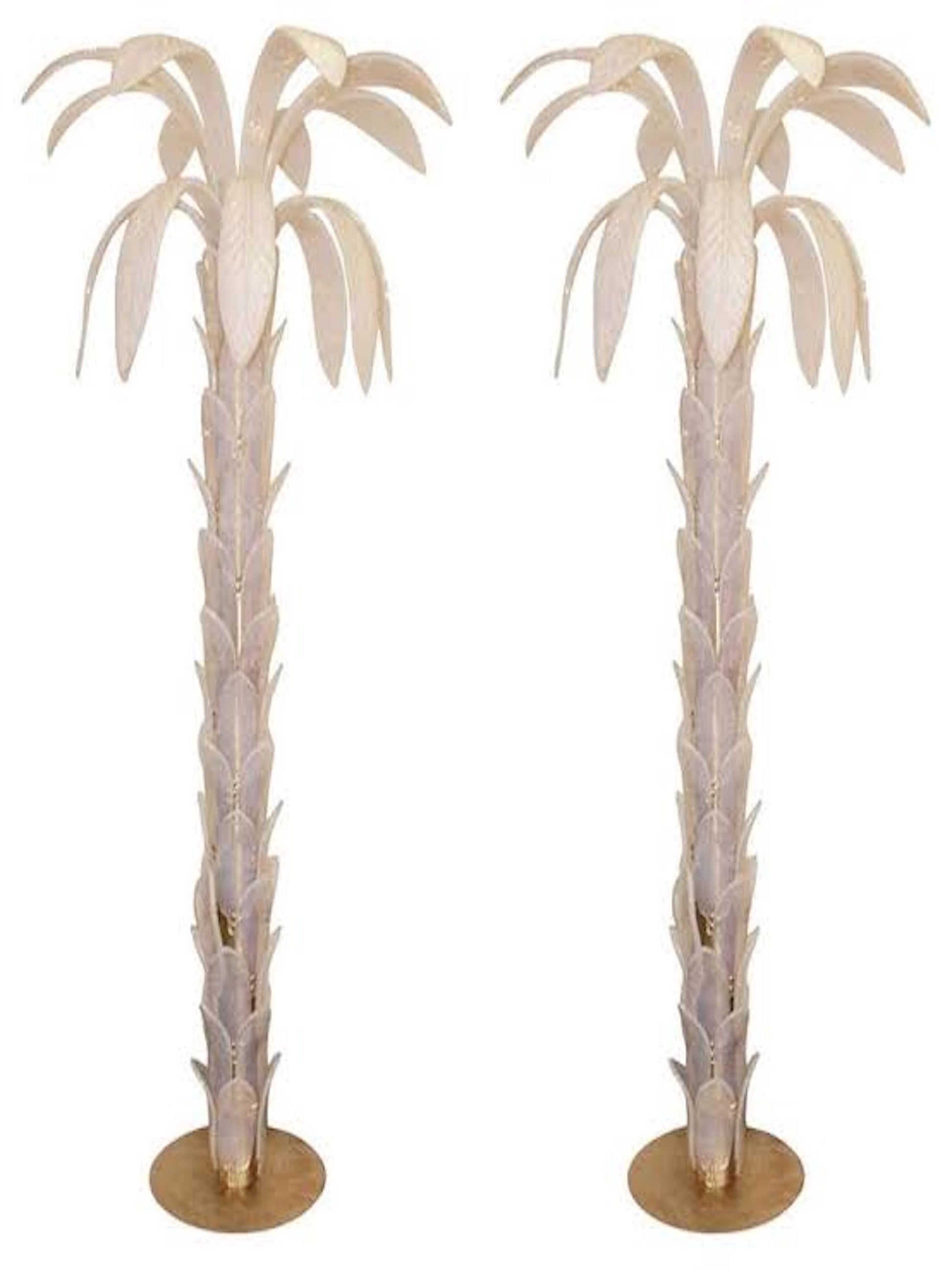 Two large white-transparent floor lamps shaped like palm trees, with brass circular bases and iridescent Murano glass leaves. They stand side by side against a white background.