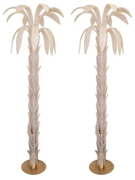 Two large white-transparent floor lamps shaped like palm trees, with brass circular bases and iridescent Murano glass leaves. They stand side by side against a white background.