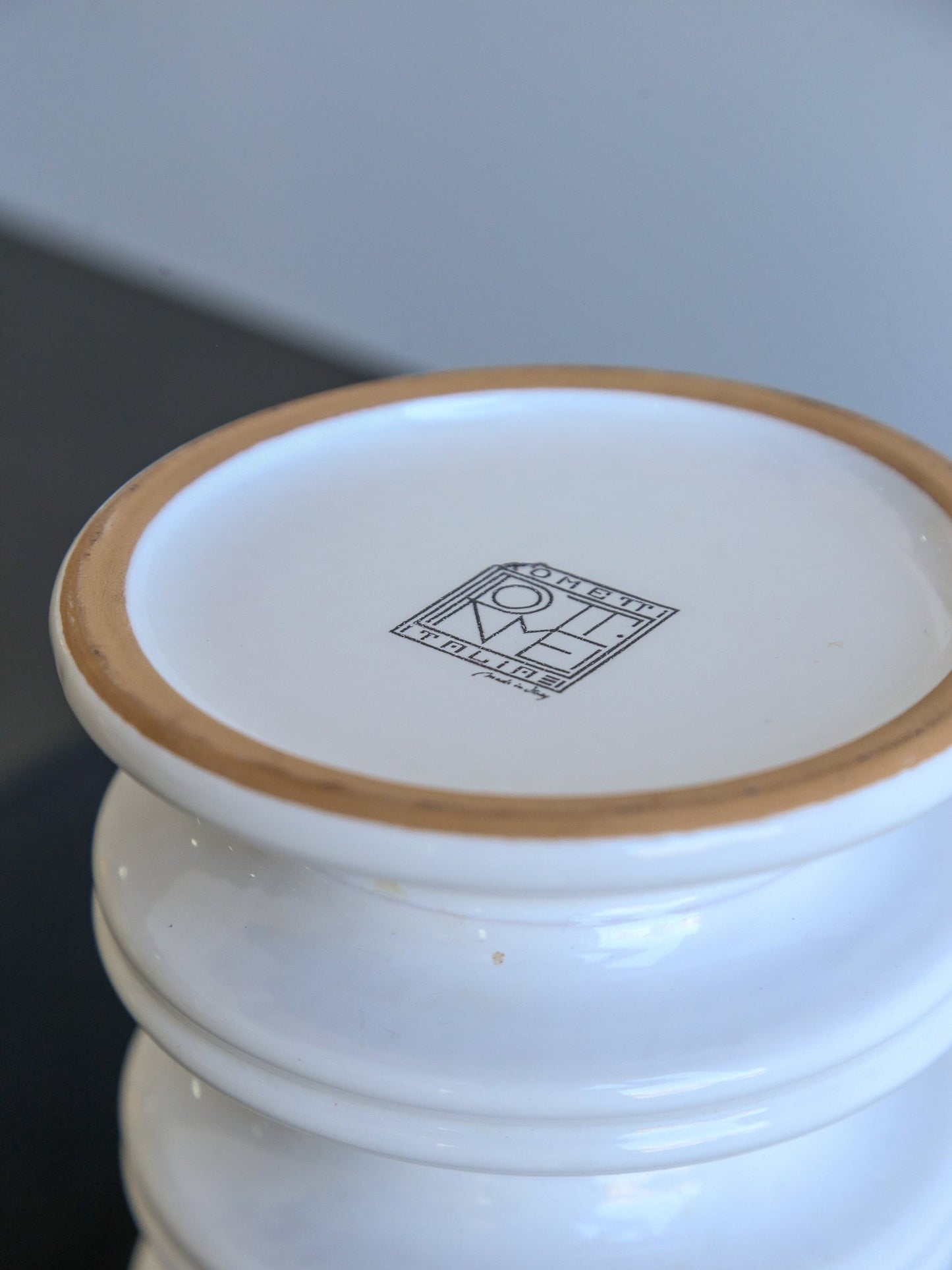 Close-up of a white ceramic container with a brown rim and a logo on a light gray background.
