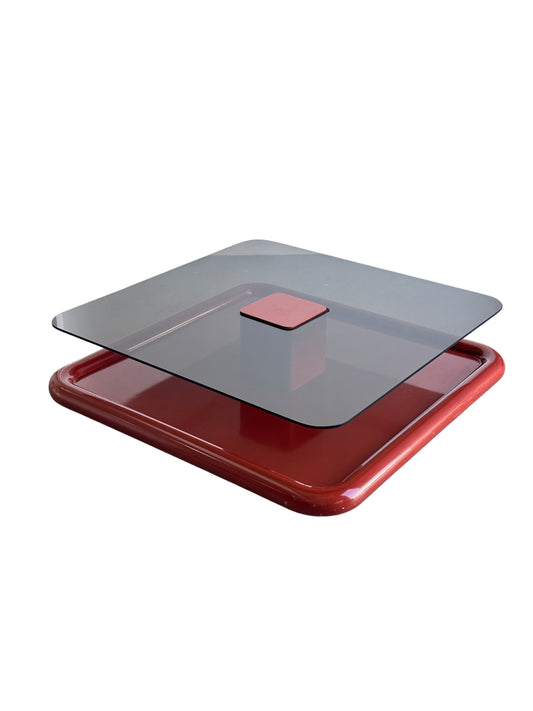 A square-shaped floating coffee table with a dark red metal base and smoked glass top designed by Marzio Cecchi for Studio Most, photographed on a white background.