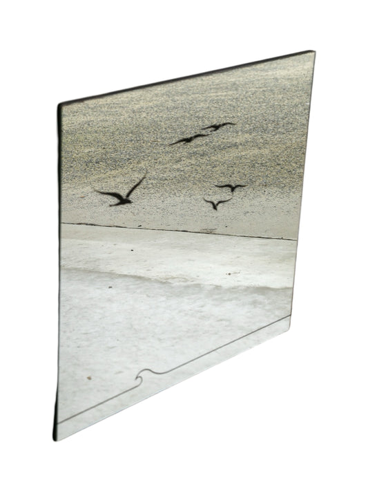 An asymmetrical, beveled wall mirror with etched silhouettes of birds in flight and a grooved detail along the bottom edge.