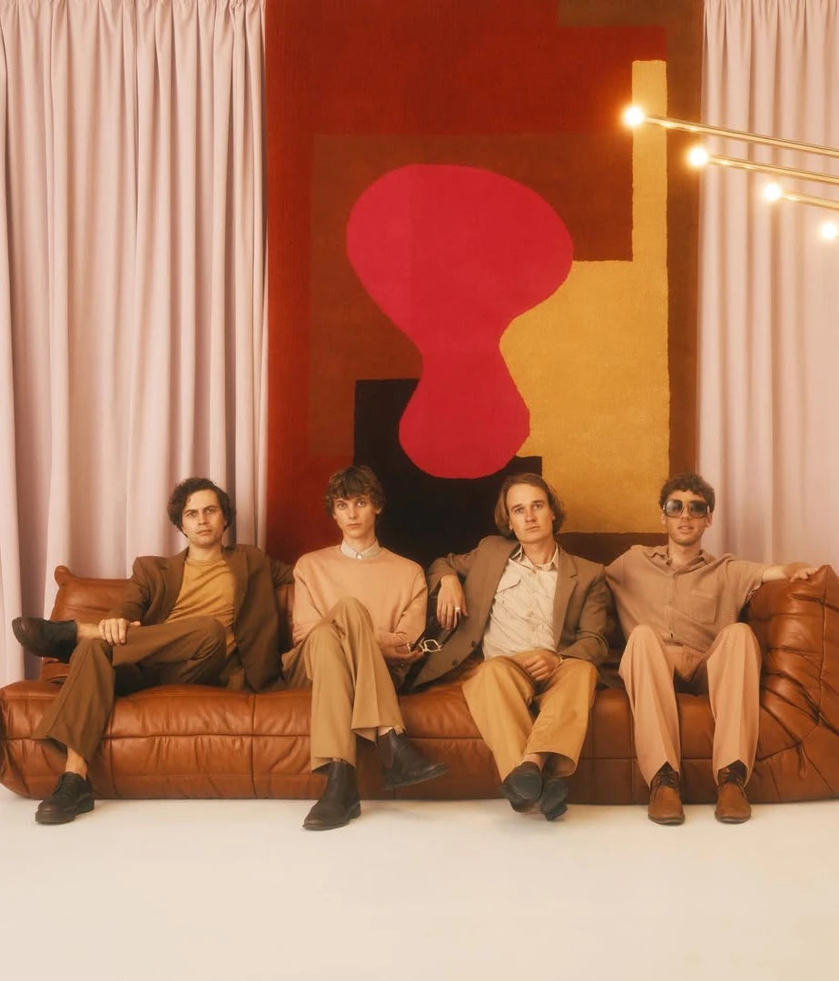 Four men sitting on a brown leather couch in a room with a large abstract painting in the background.