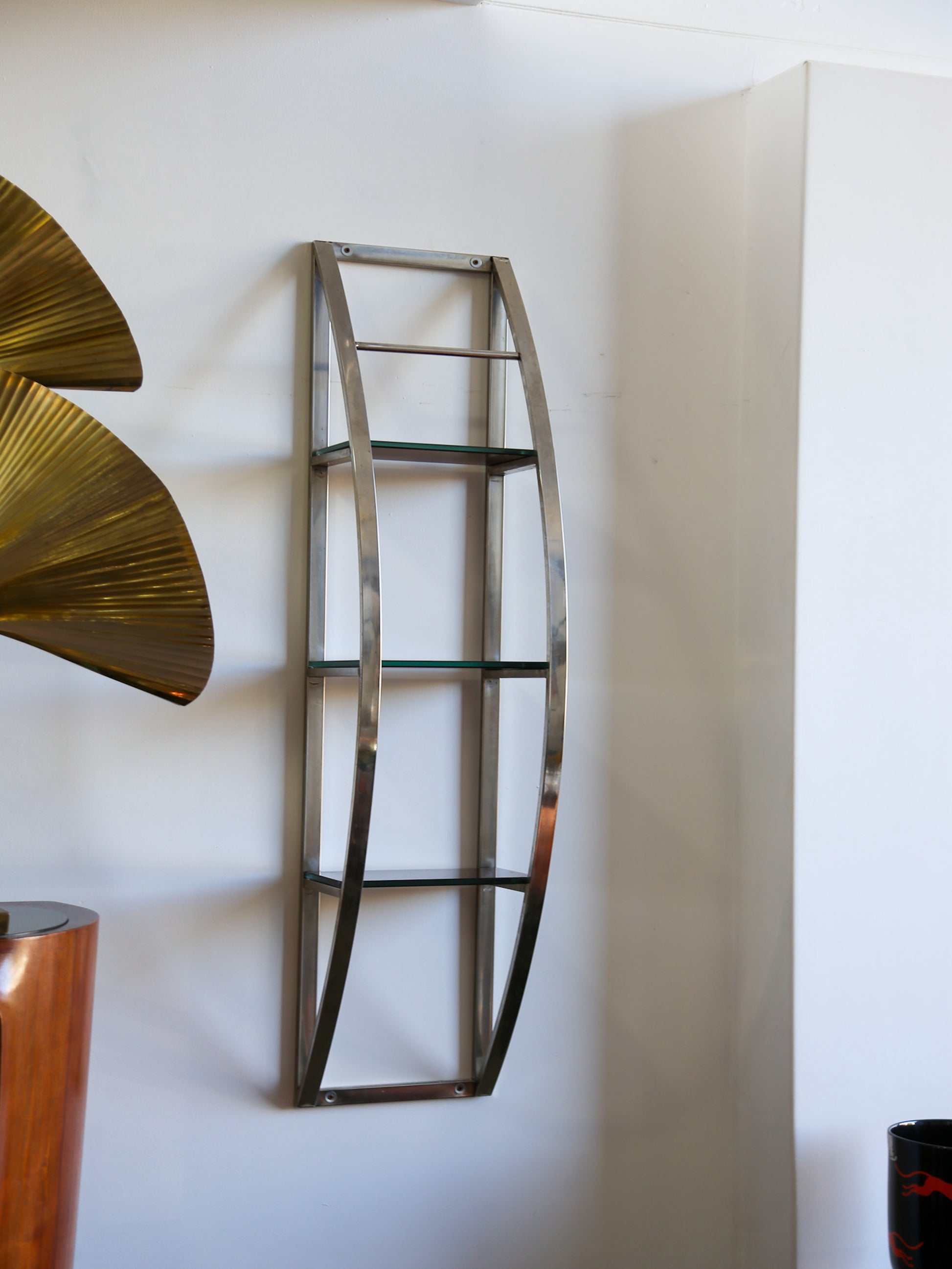 Wide shot of Italian vintage chrome and glass shelf in interior setting with brass fan sculpture