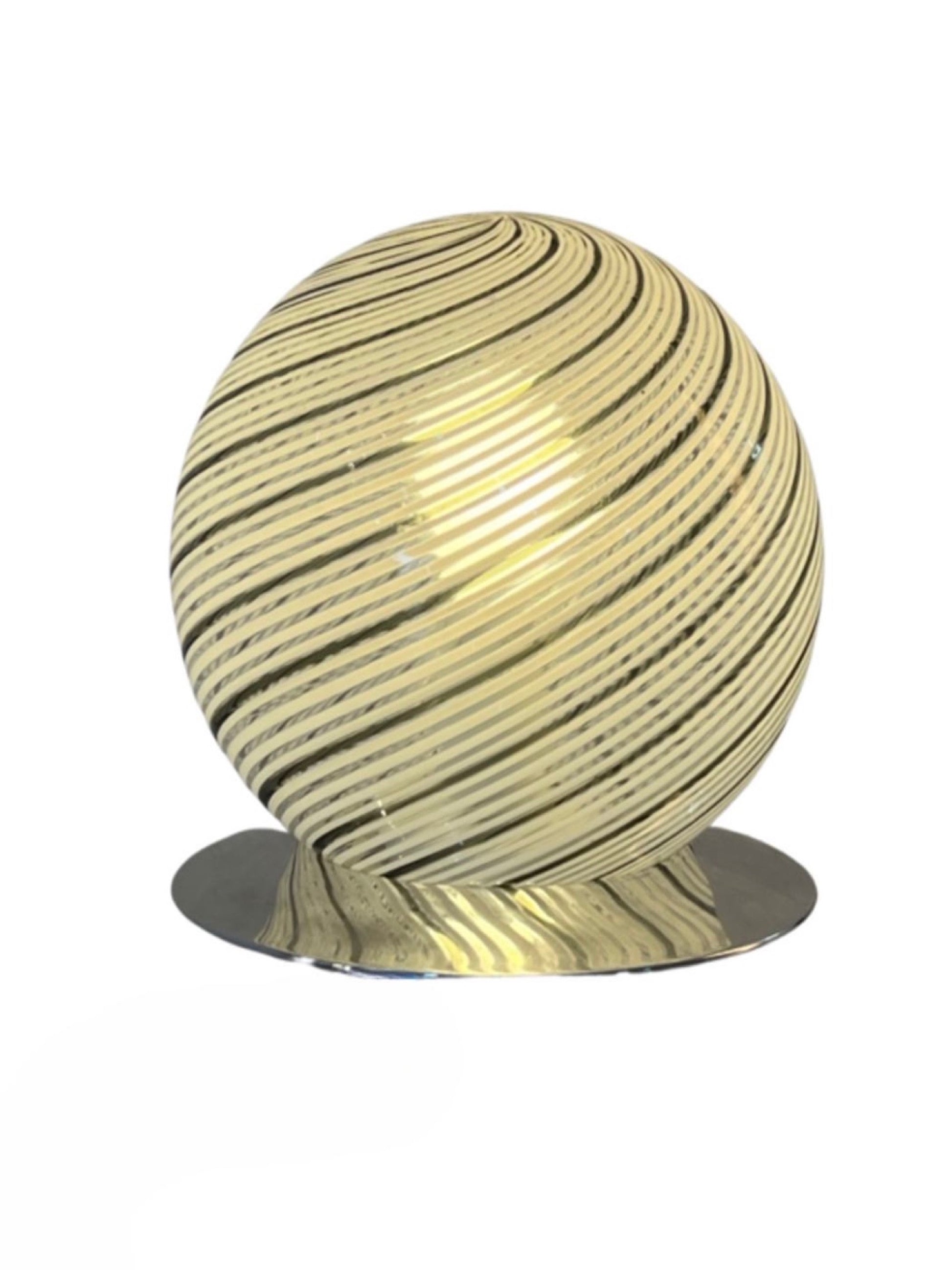 A spherical Murano glass table lamp with a chrome base, featuring a textured surface with stripes in a gold color, emitting a warm light by Tronconi