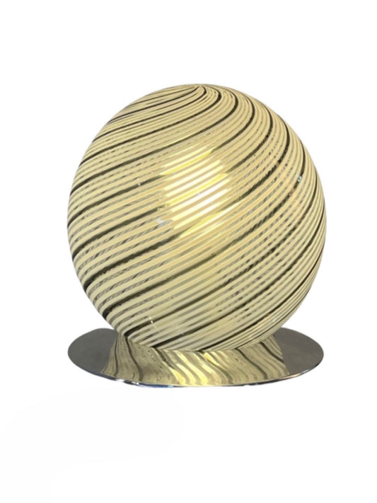 A spherical Murano glass table lamp with a chrome base, featuring a textured surface with stripes in a gold color, emitting a warm light by Tronconi