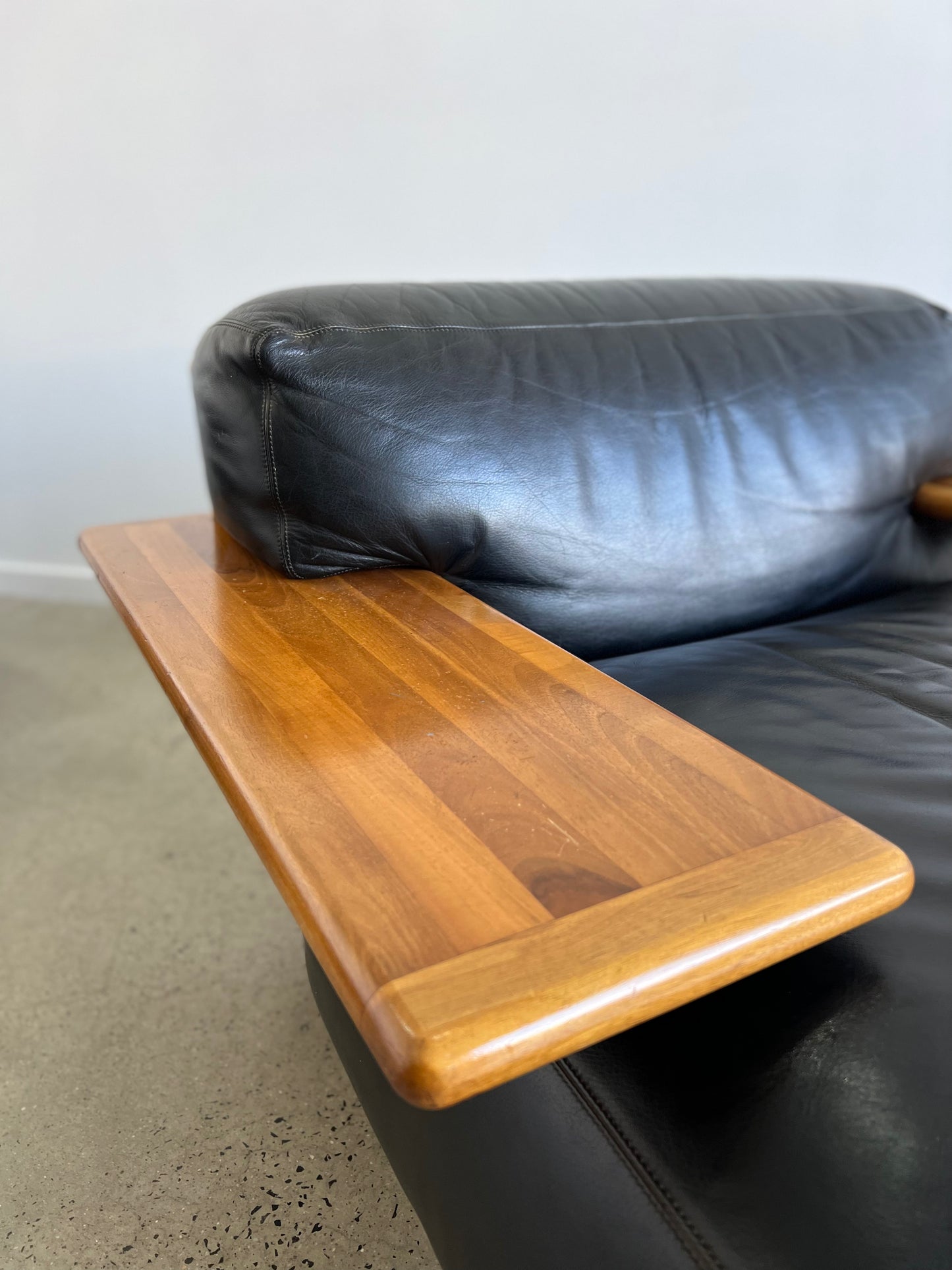 Detail of Pianura lounge chair by Mario Bellini for Cassina, 1970, showing walnut armrest, black leather upholstery, and sculptural design.