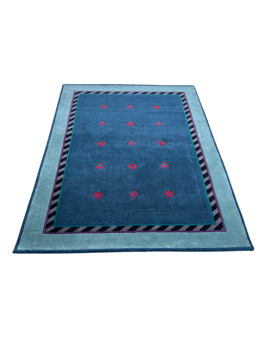 A rectangular dark green wool carpet with a pattern of organic shapes and lines in a subtle design, with a blue border and red accents.