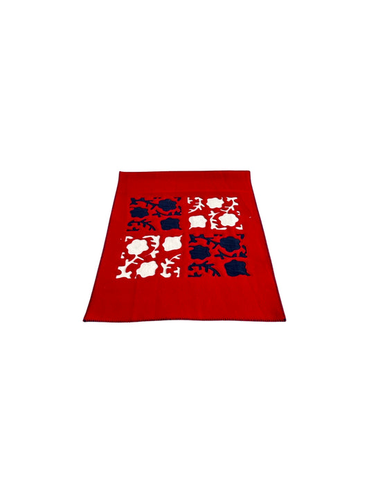 A red wool rug with a large abstract flower design in shades of red and pink, by Paola Lenti.
