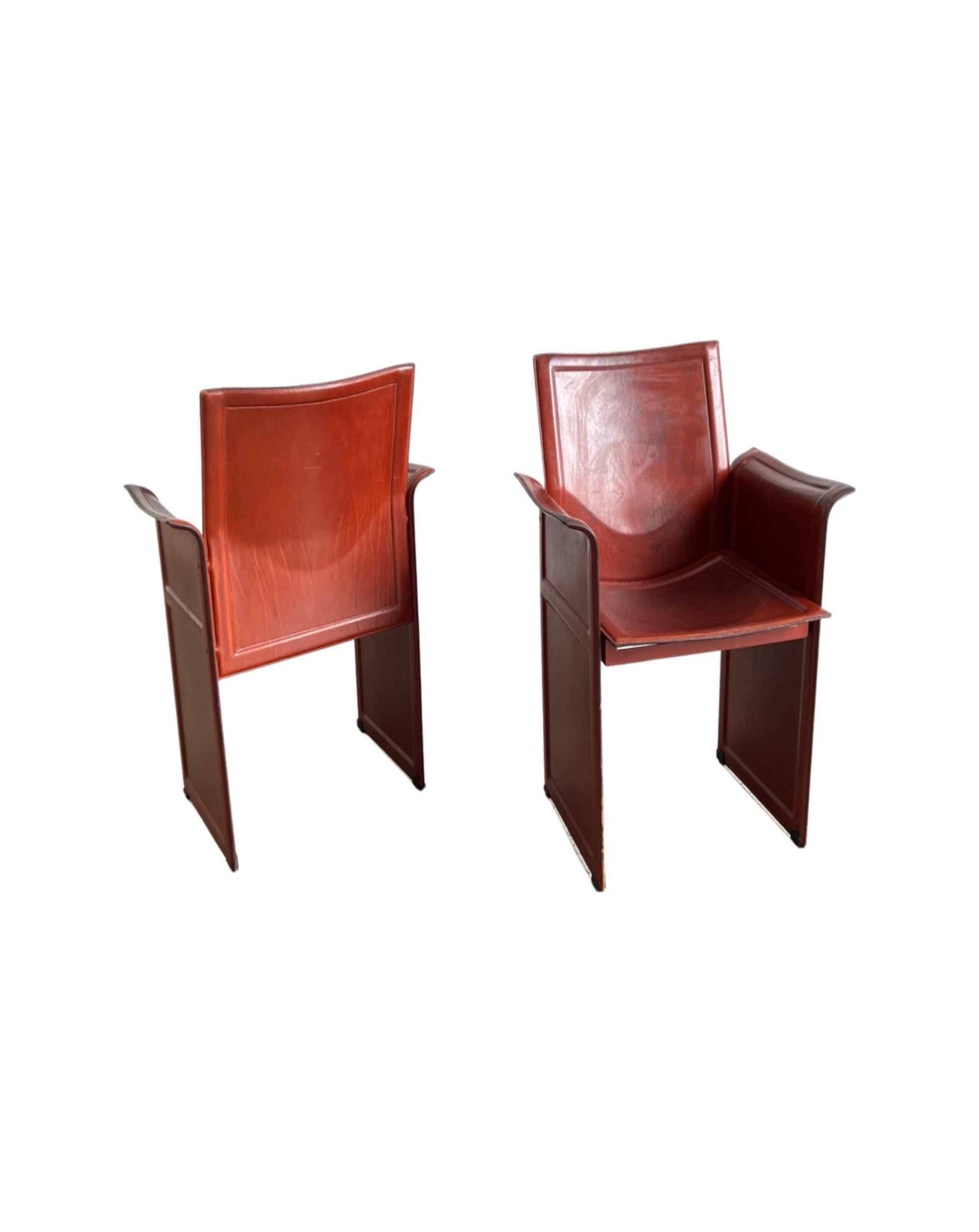 A pair of brown 'Korium' leather armchairs designed by Tito Agnoli for Matteo Grassi, featuring a full leather upholstery and wooden frame.