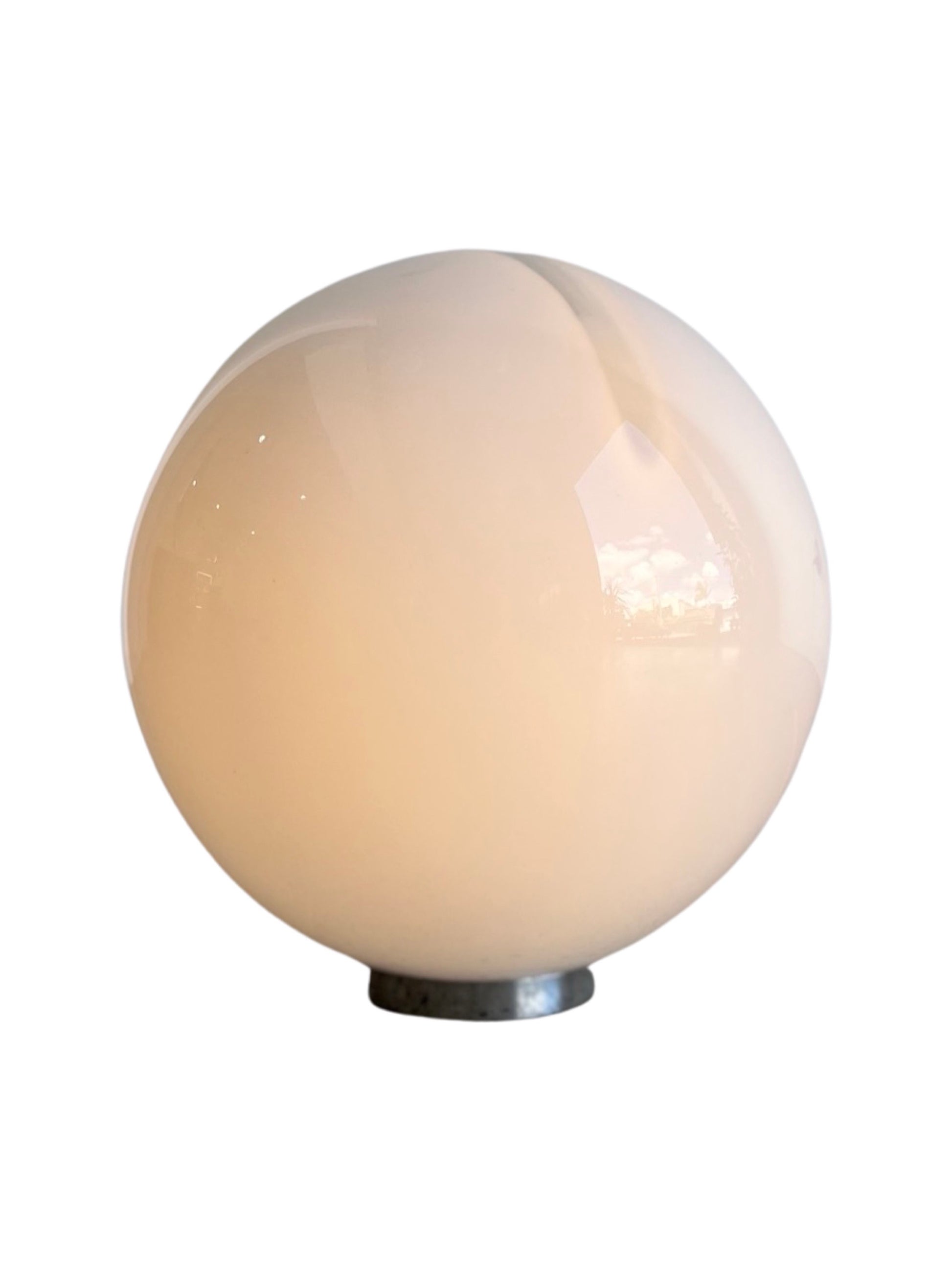 A spherical white glass table lamp with a chrome base, reflecting light on its surface by Alfredo Barbini