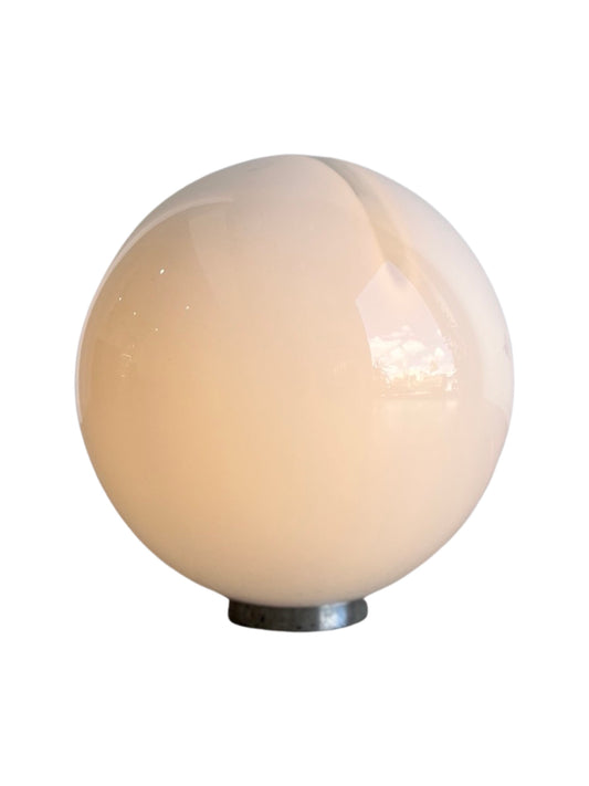 A spherical white glass table lamp with a chrome base, reflecting light on its surface by Alfredo Barbini