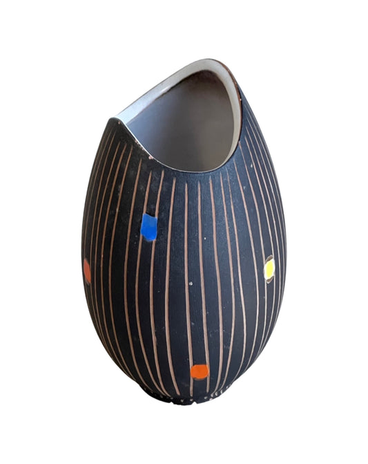 A small black ceramic vase with hand painted stripes and multicolored dots.