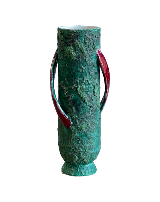 A light green ceramic vase with a textured surface and red accents, standing with a lopsided shape.