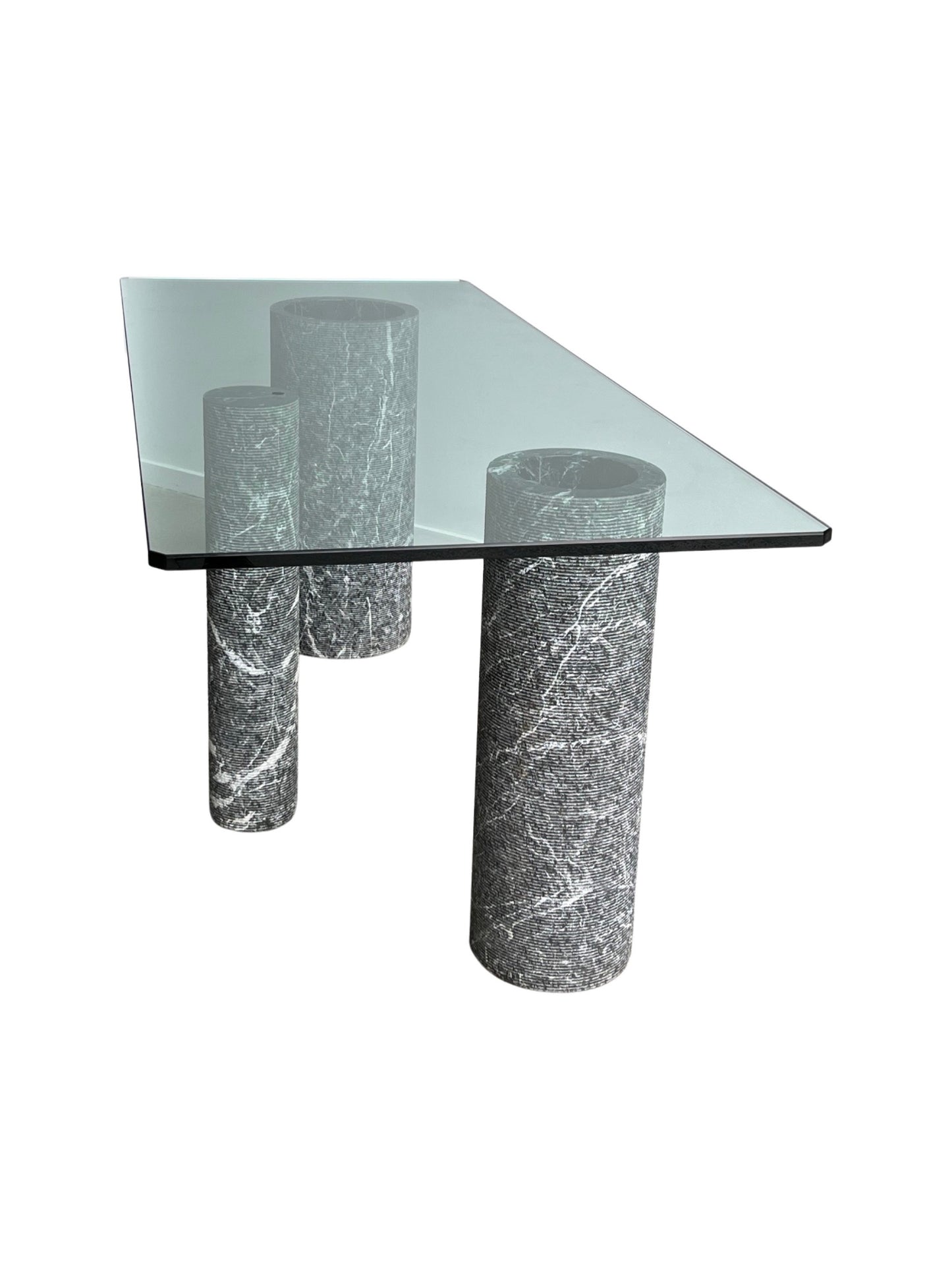 A rectangular dining table with a glass top and marble columns in varying diameters with a rough texture finish by Massimo Vignelli for Casigliani