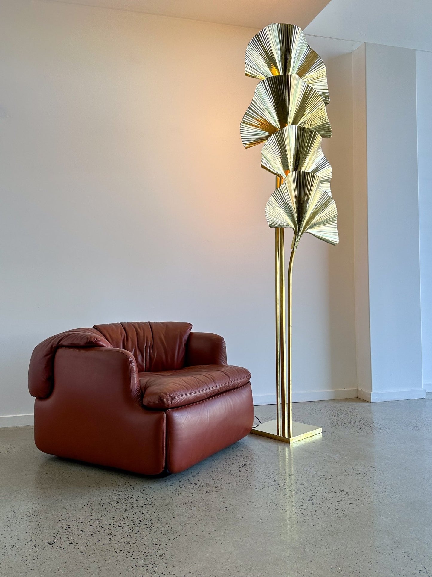 Modern brown leather armchair next to a gold floor lamp in a minimalistic room.