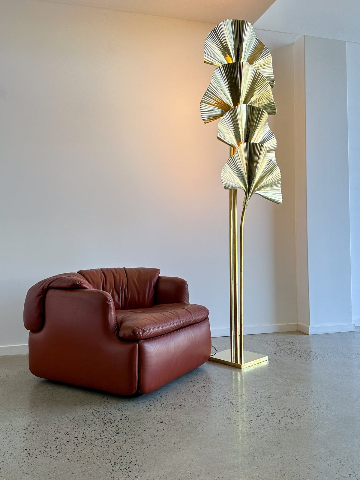Modern brown leather armchair next to a gold floor lamp in a minimalistic room.