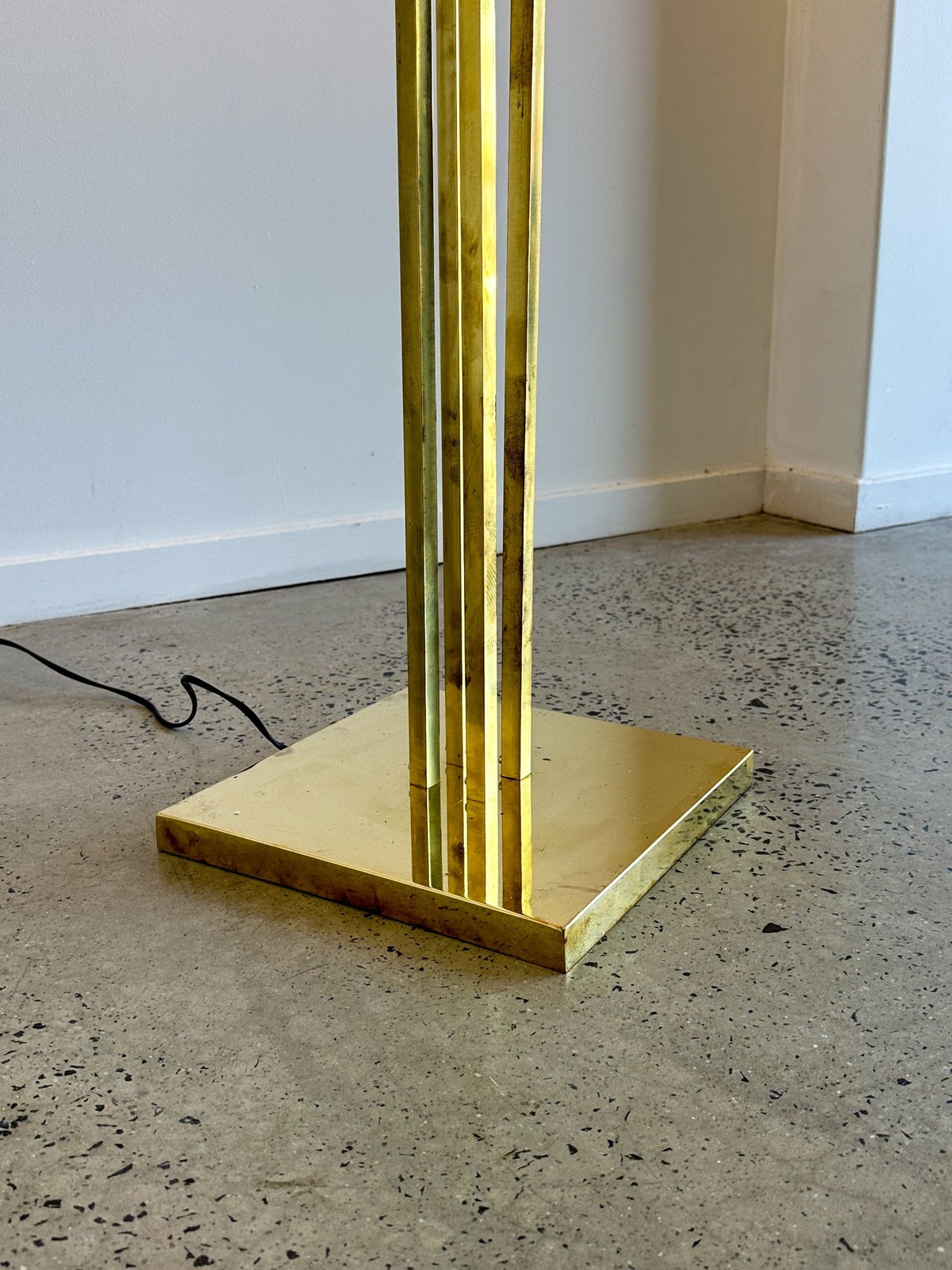 Gold floor lamp with a square base on a speckled floor.