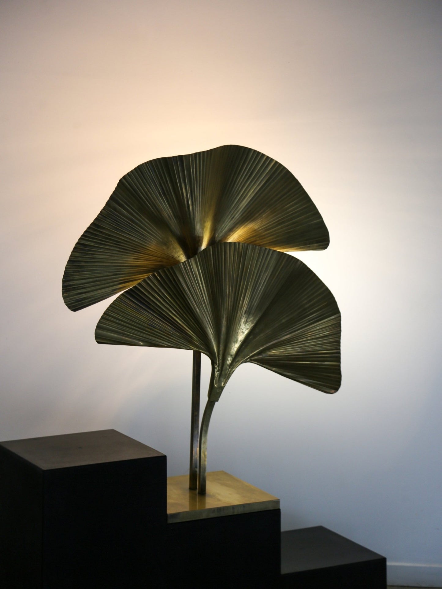 Decorative leaf-shaped lamp on a black pedestal against a white wall