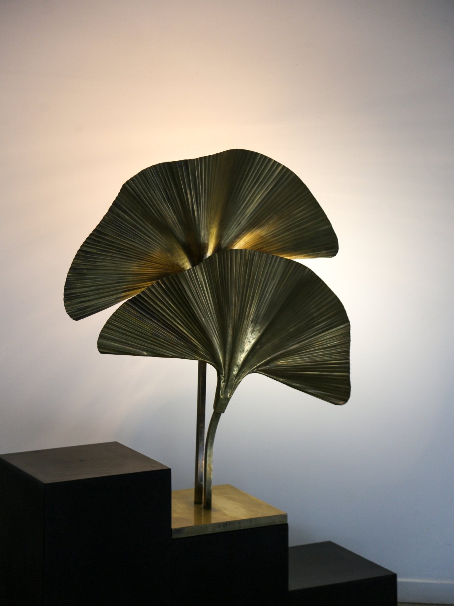 Decorative leaf-shaped lamp on a black pedestal against a white wall