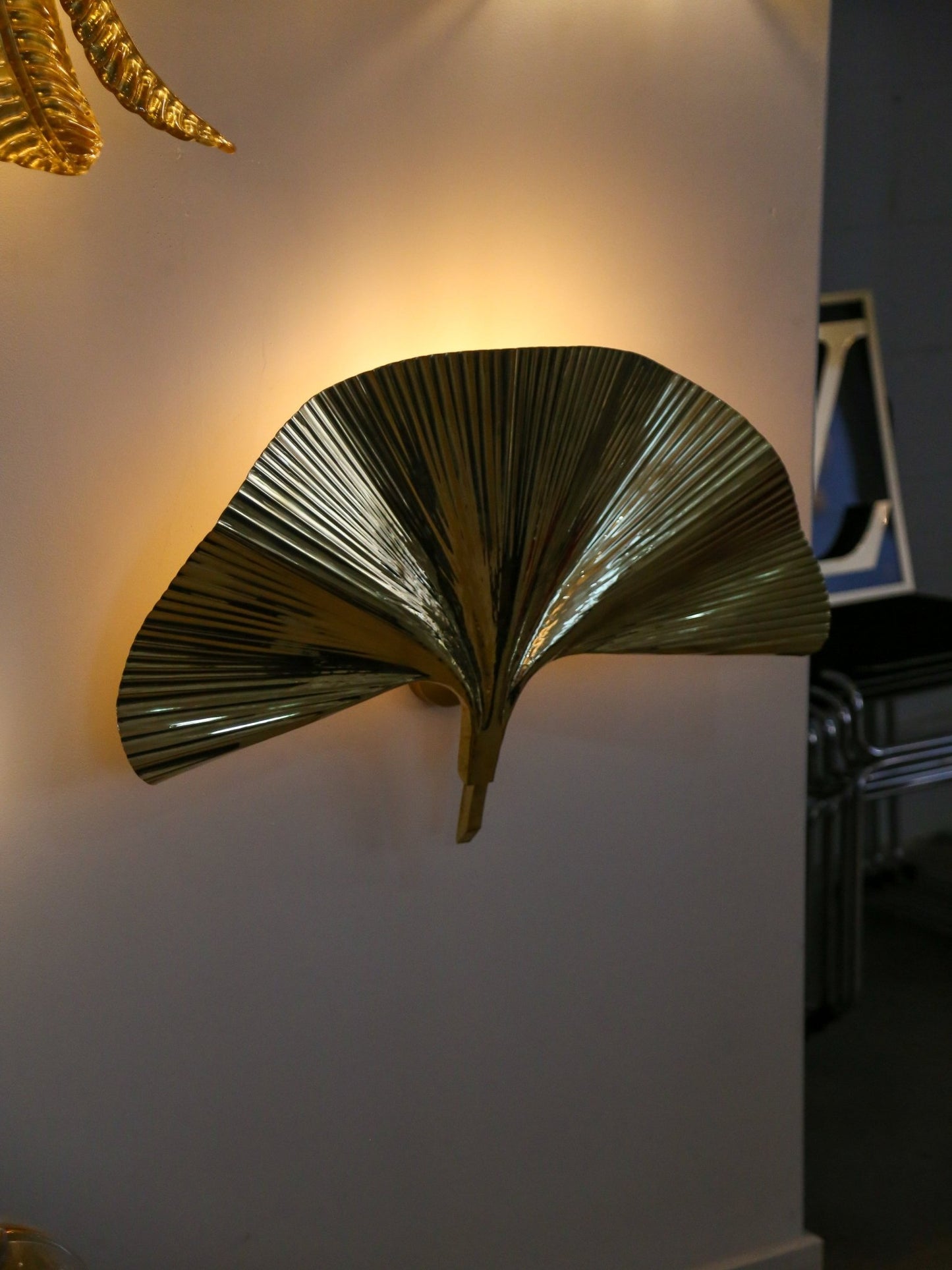 Decorative wall sconce shaped like a palm leaf on a white wall.