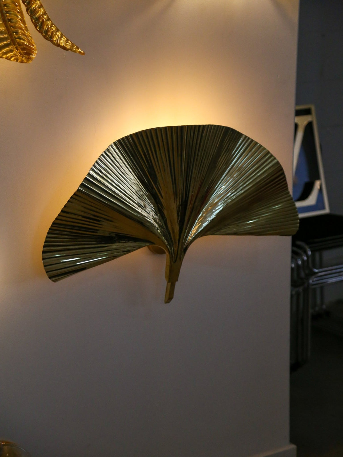 Decorative wall sconce shaped like a palm leaf on a white wall.