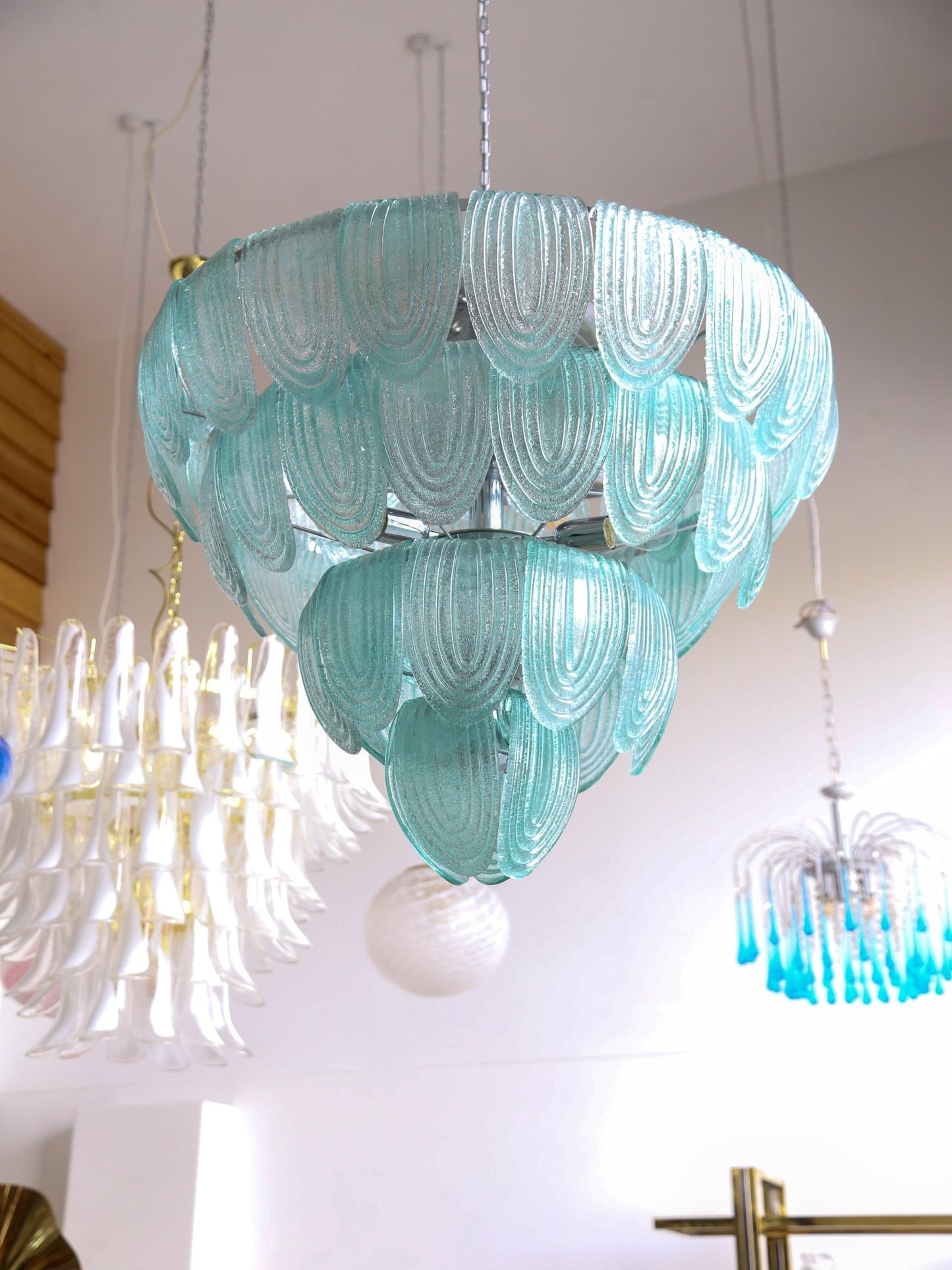 Turquoise glass chandelier hanging in a room with other chandeliers.