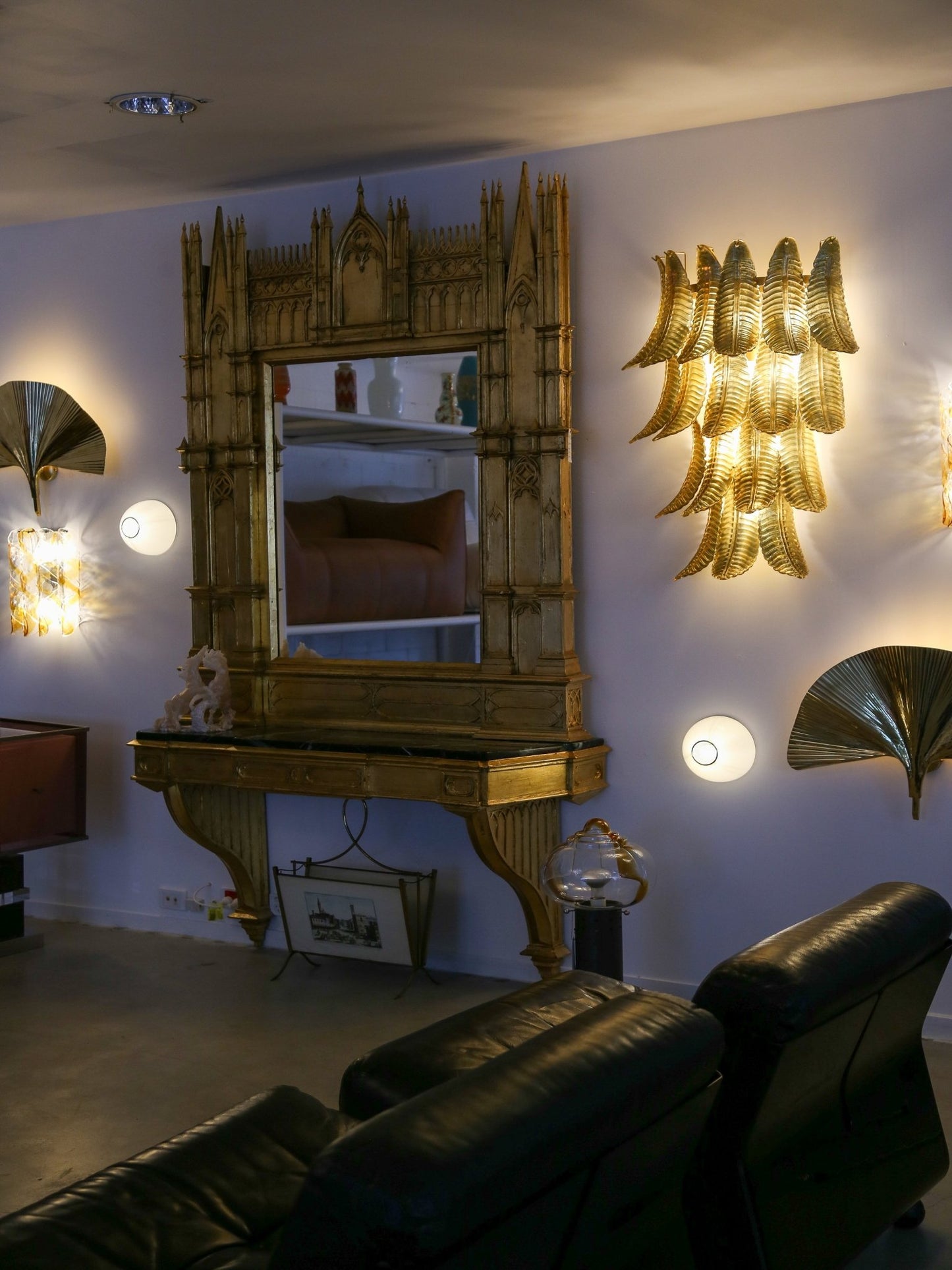 Living room with ornate mirror, wall sconces, and black leather sofa.