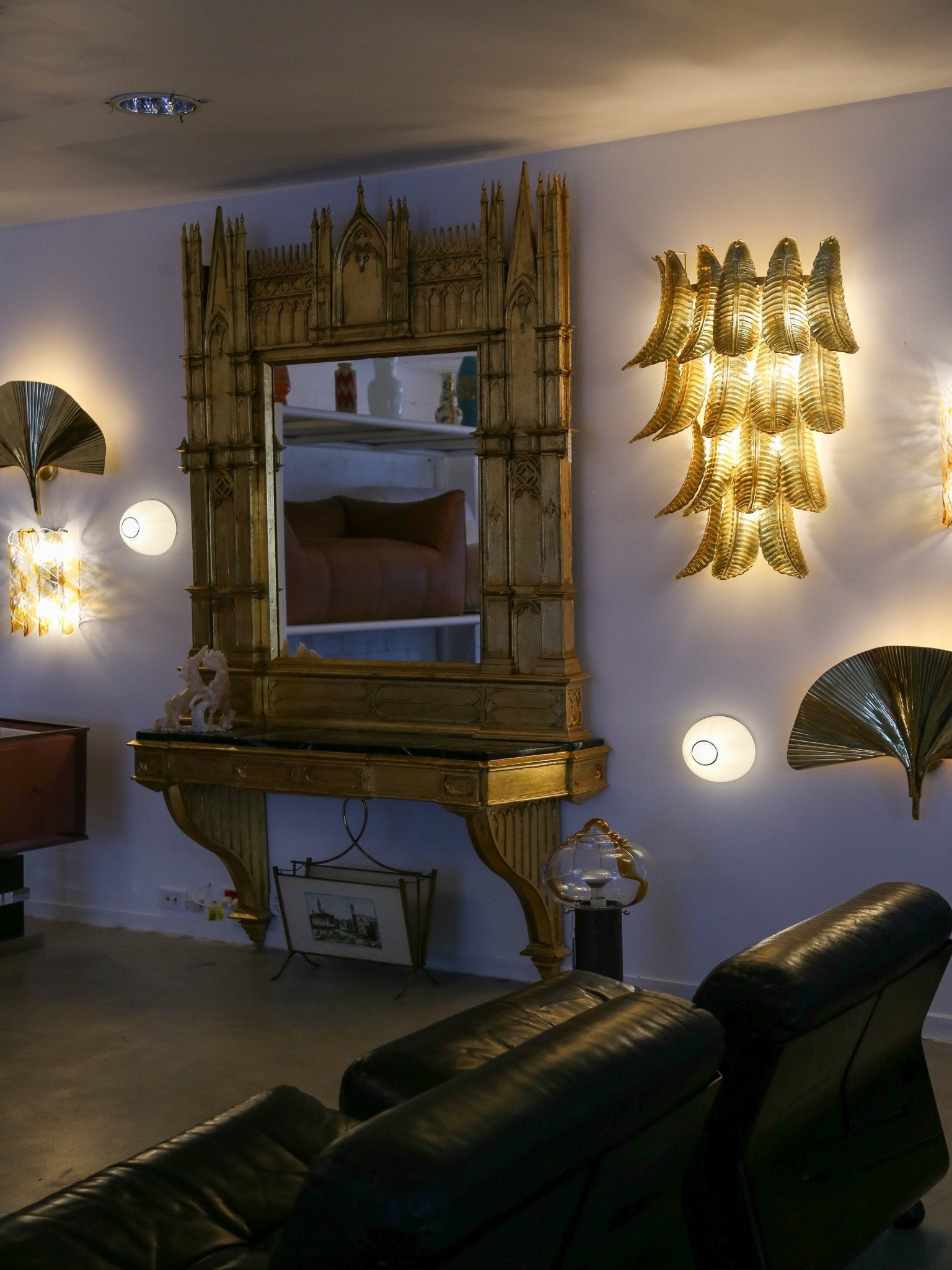 Living room with ornate mirror, wall sconces, and black leather sofa.