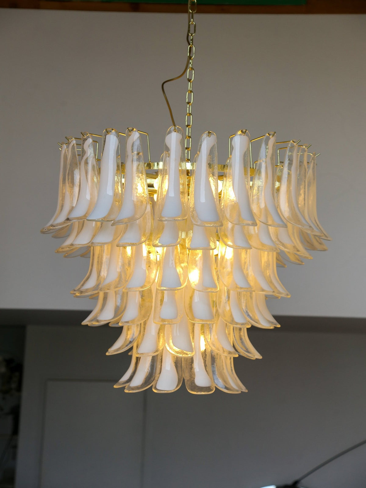 Vintage chandelier with white glass shades and gold metal frame against a plain wall.