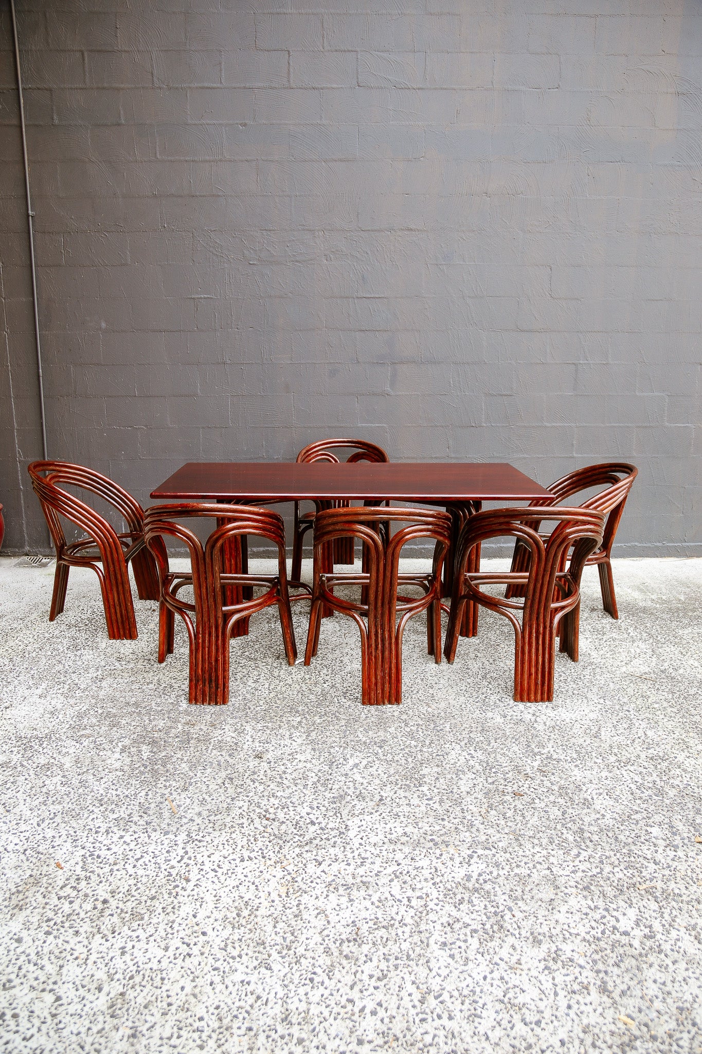 A mid-century modern bentwood dining set consisting of a rectangular table and six matching chairs, shown against a gray brick wall and speckled concrete floor.