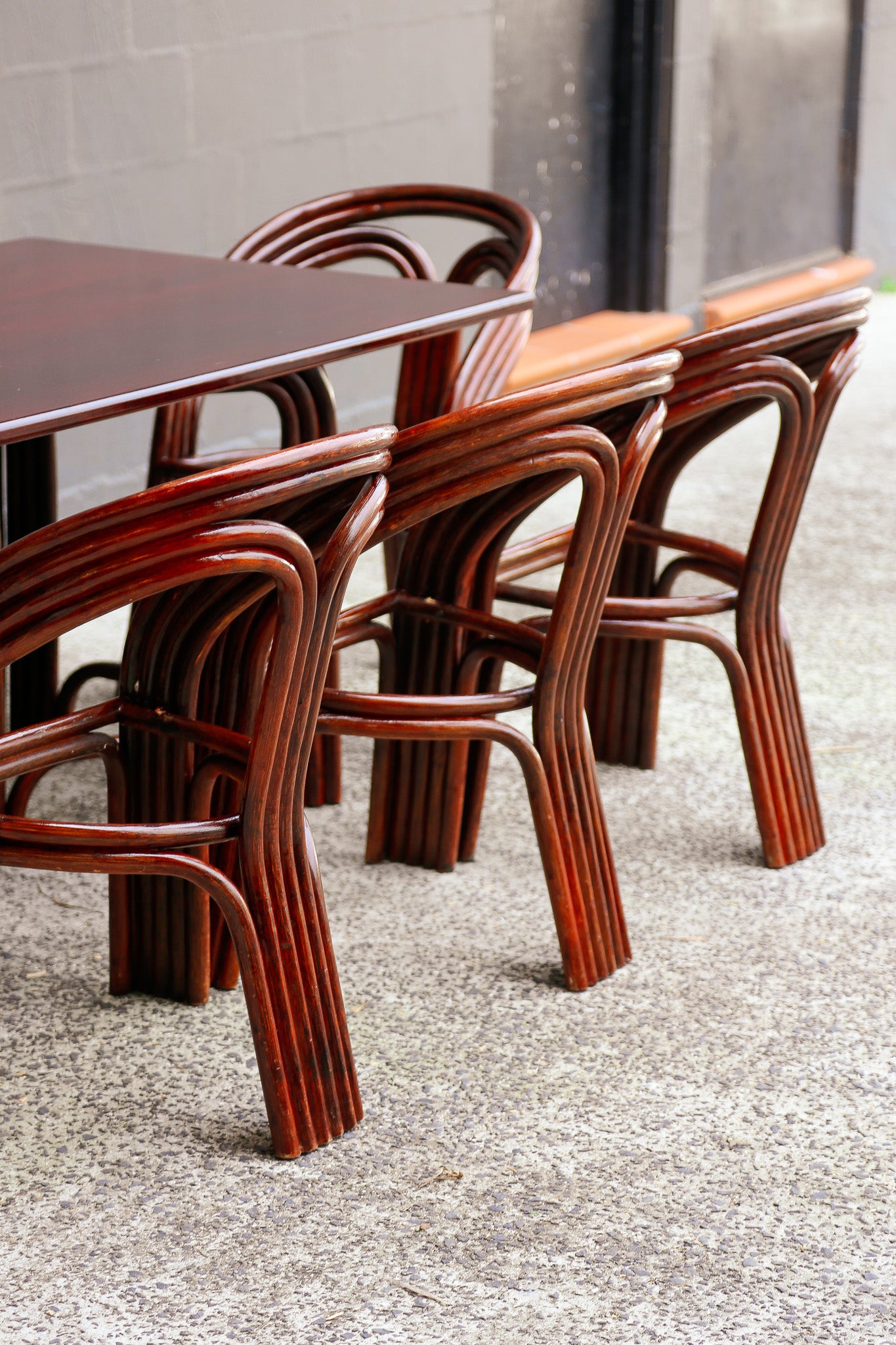A set of curved bentwood dining chairs with reddish-brown wooden seats, arranged around a matching wooden table on a speckled concrete floor.