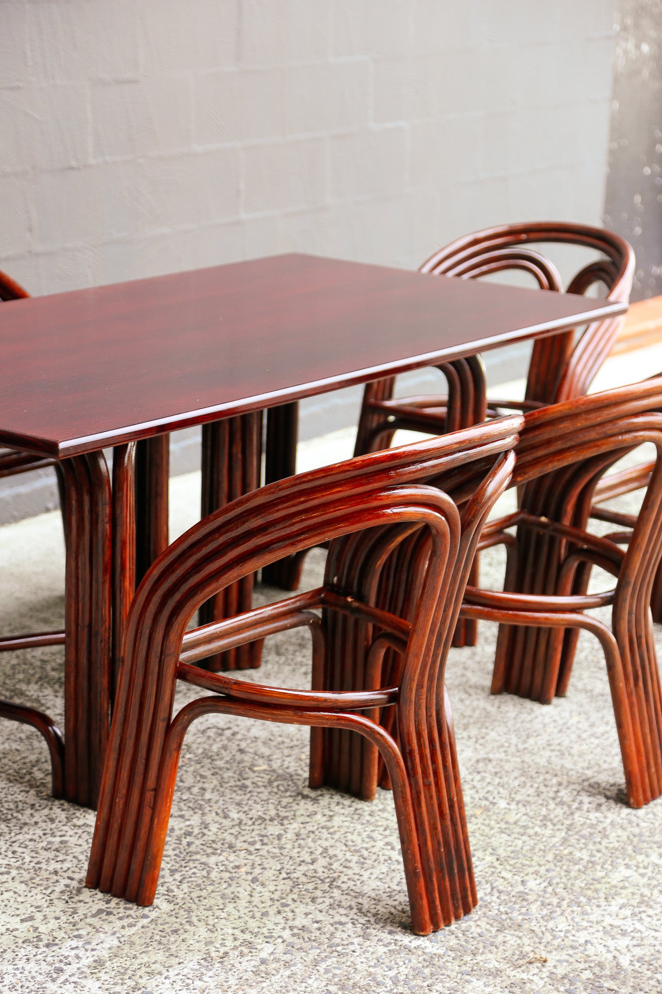 A dark reddish-brown wooden dining table with matching curved bentwood chairs, set in an indoor space with a gray tiled floor and light gray brick wall.