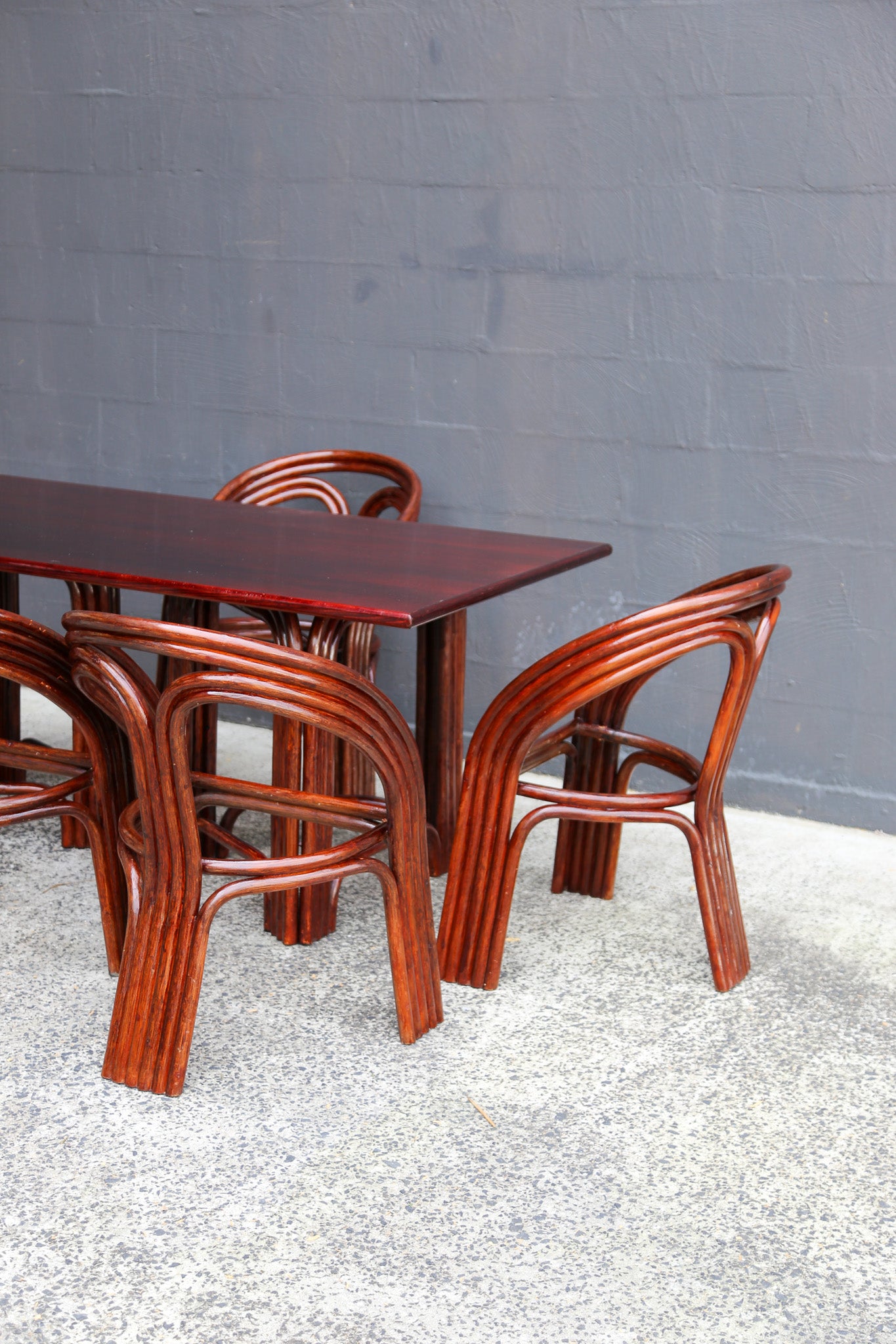 A set of mid-century modern bentwood dining furniture, including a rectangular table and four matching chairs with curved, ribbed legs, shown against a gray brick wall and concrete floor.
