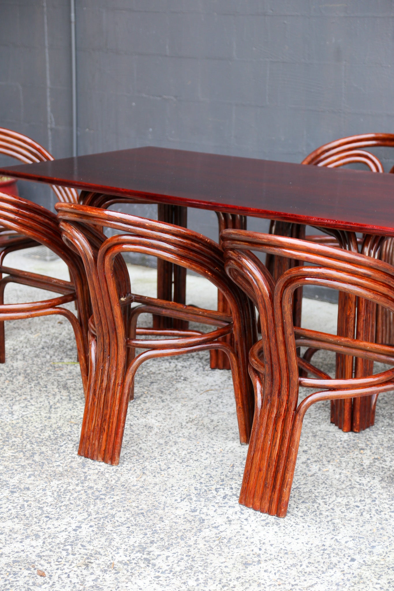 A dark reddish-brown wooden dining table with matching curved wooden chairs, set against a gray brick wall and speckled concrete floor.