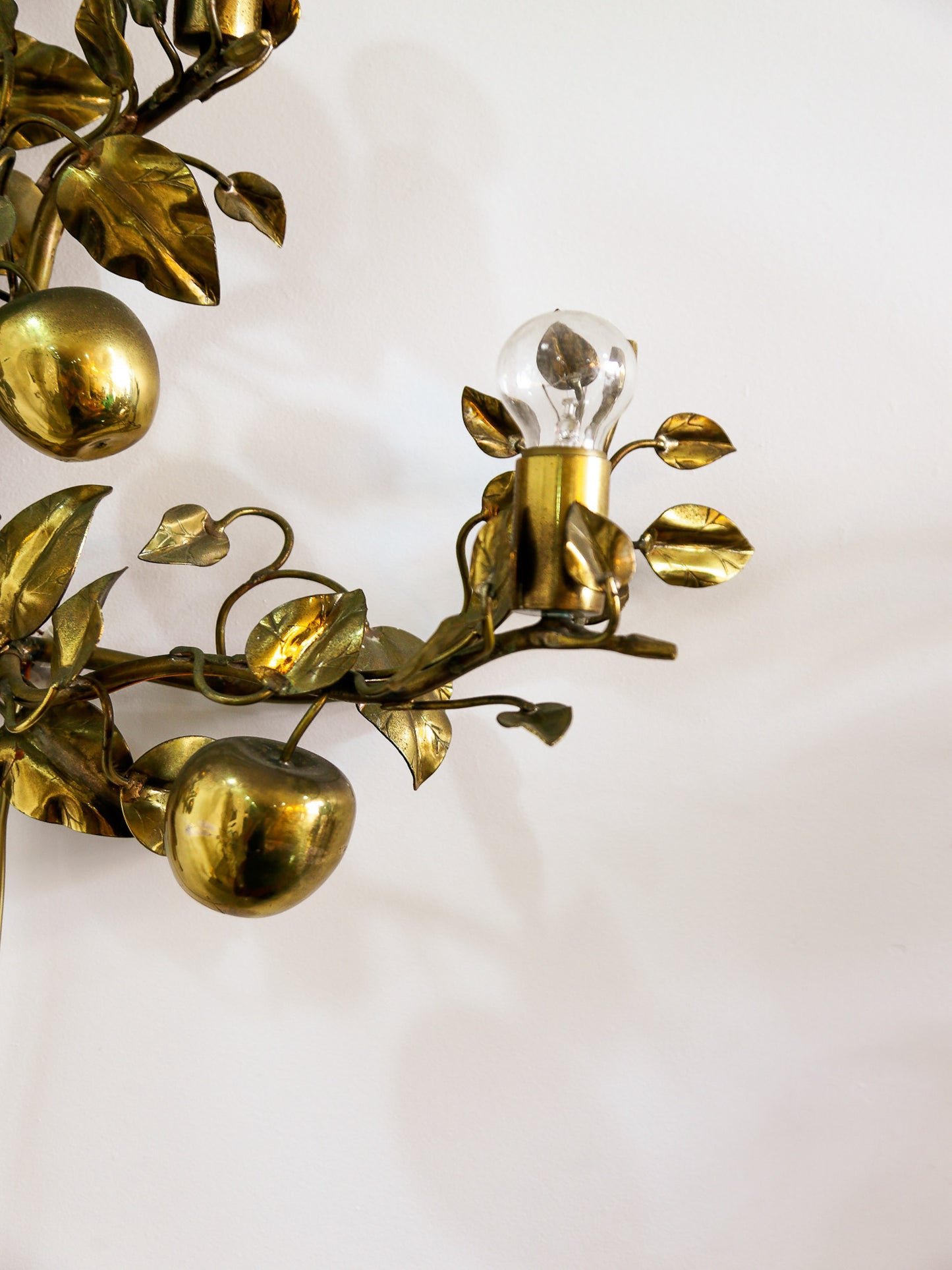 Brass wall sconce with leaf and apple design on a white background