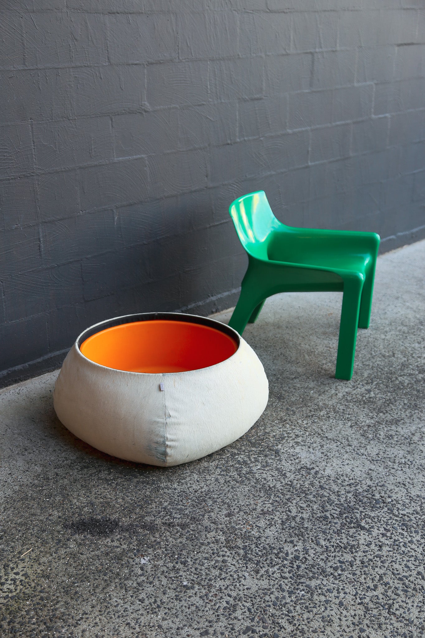 White and orange bean bag chair next to a green chair against a gray wall.
