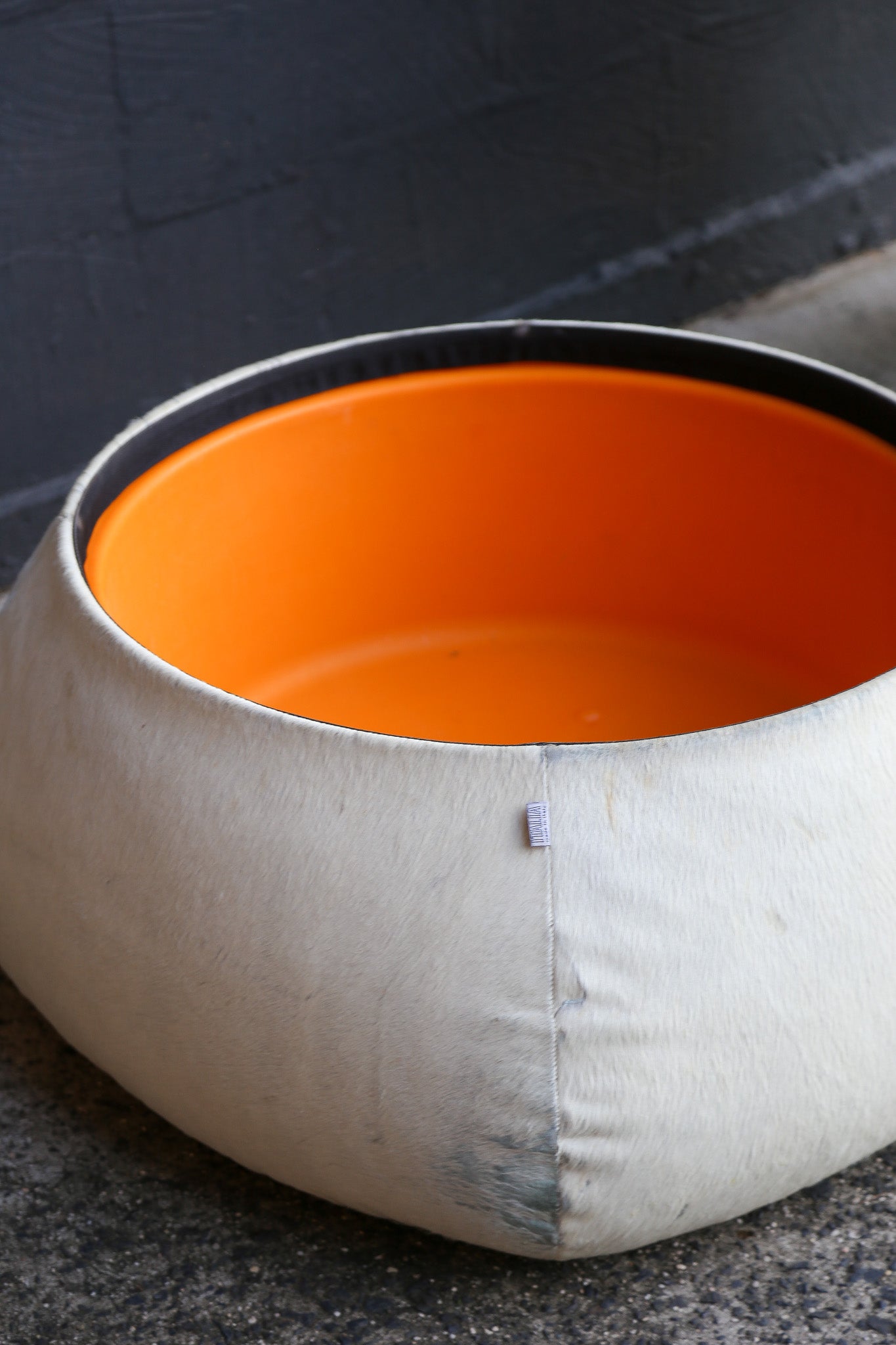 Round white pet bed with an orange interior on a dark surface