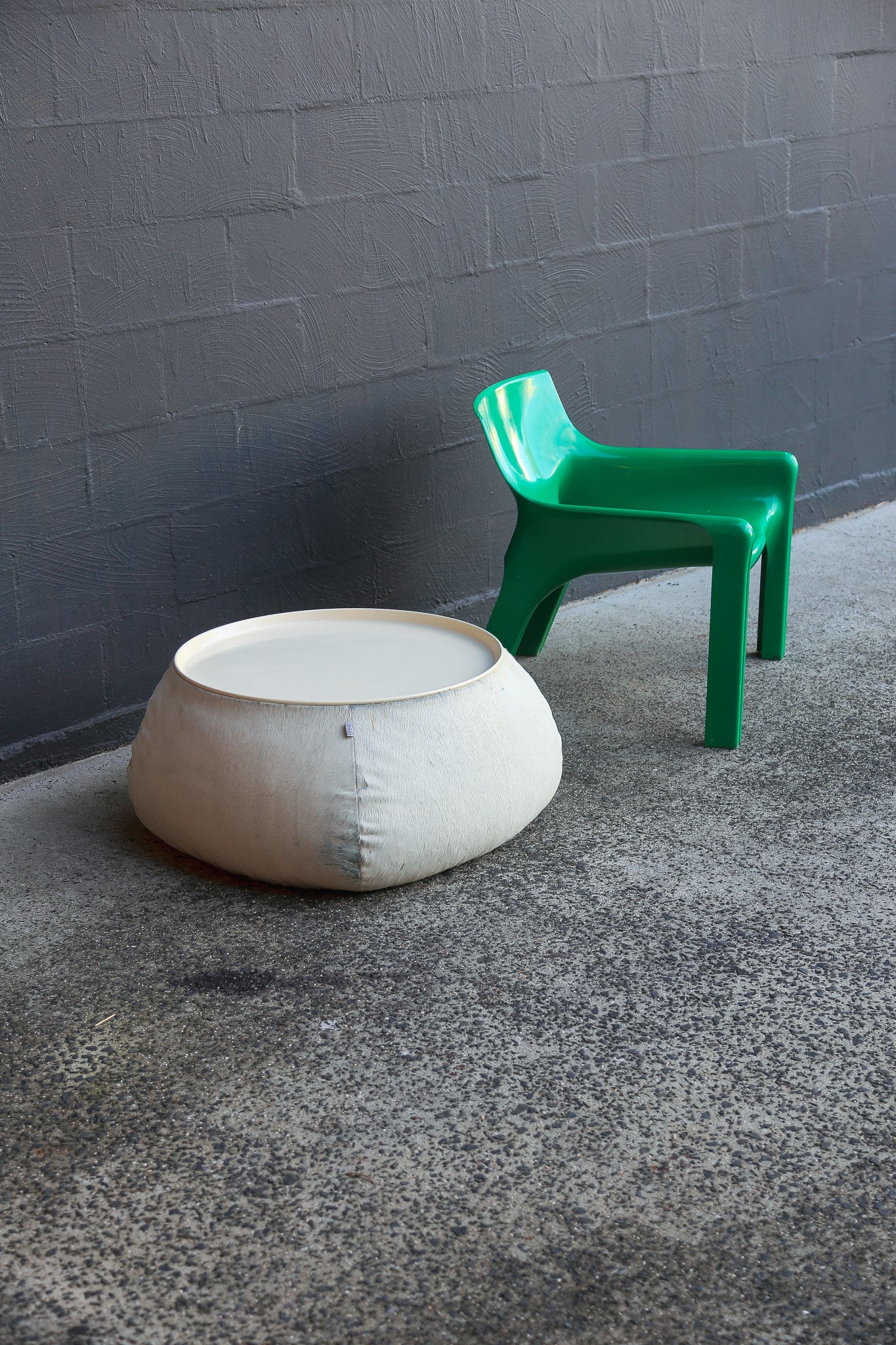 Green chair and beige ottoman on a gray floor against a gray wall