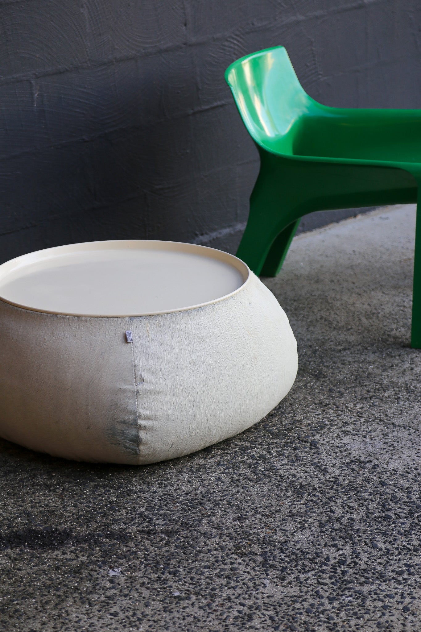 White ottoman and green chair on a gray floor with dark gray wall background