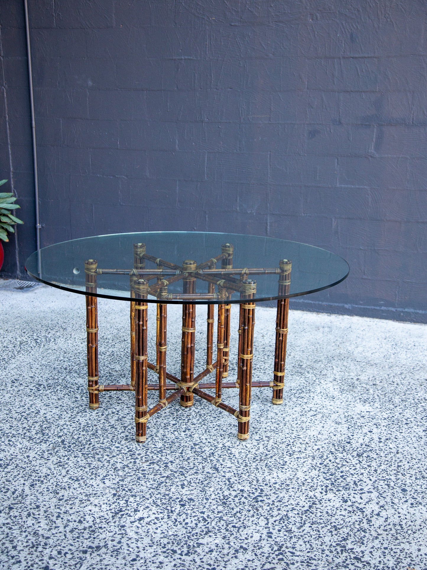 Glass dining table with bamboo-like metal frame on a textured surface with a dark wall background