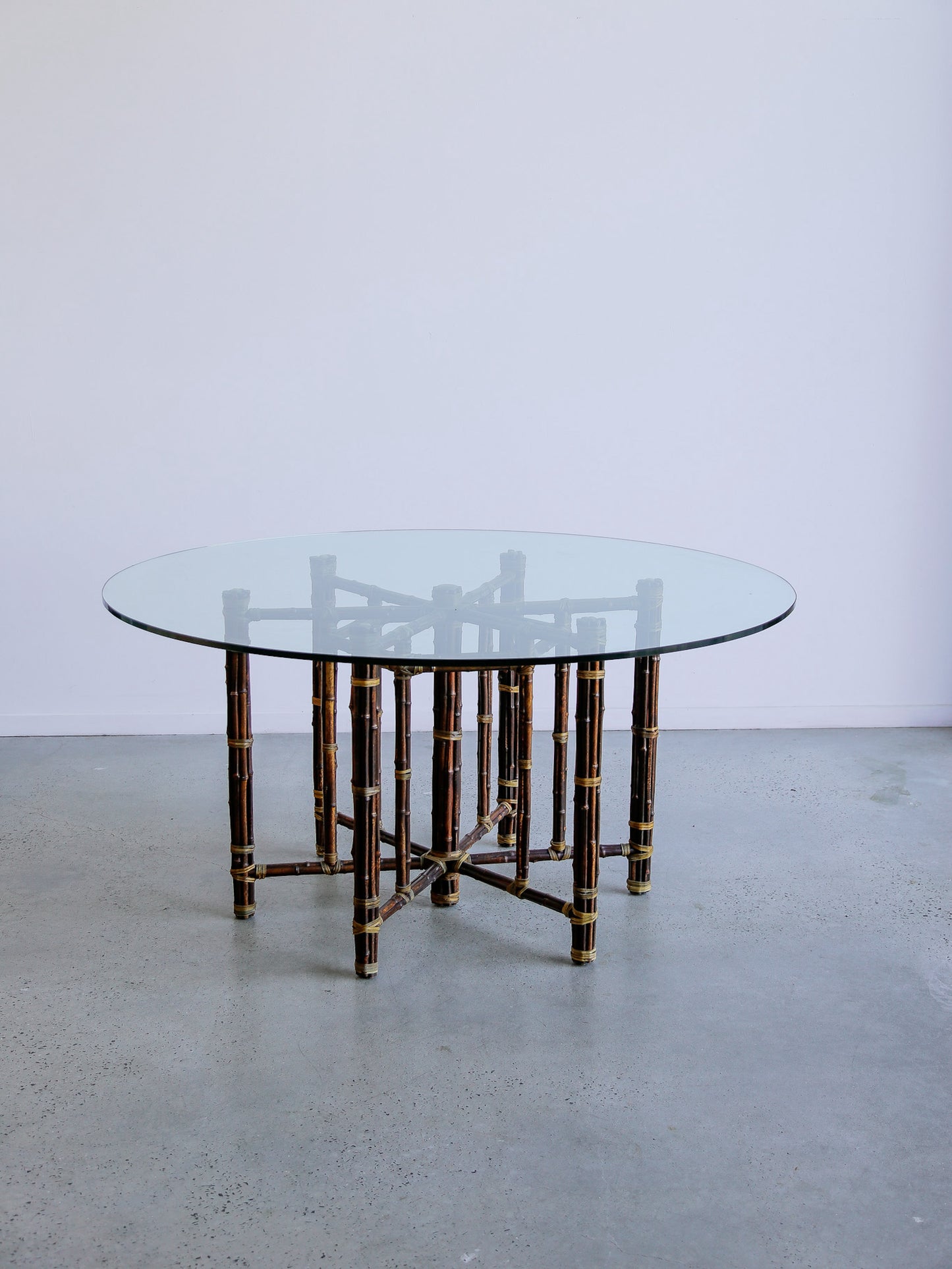 Round glass table with bamboo-style frame on a plain floor and wall background